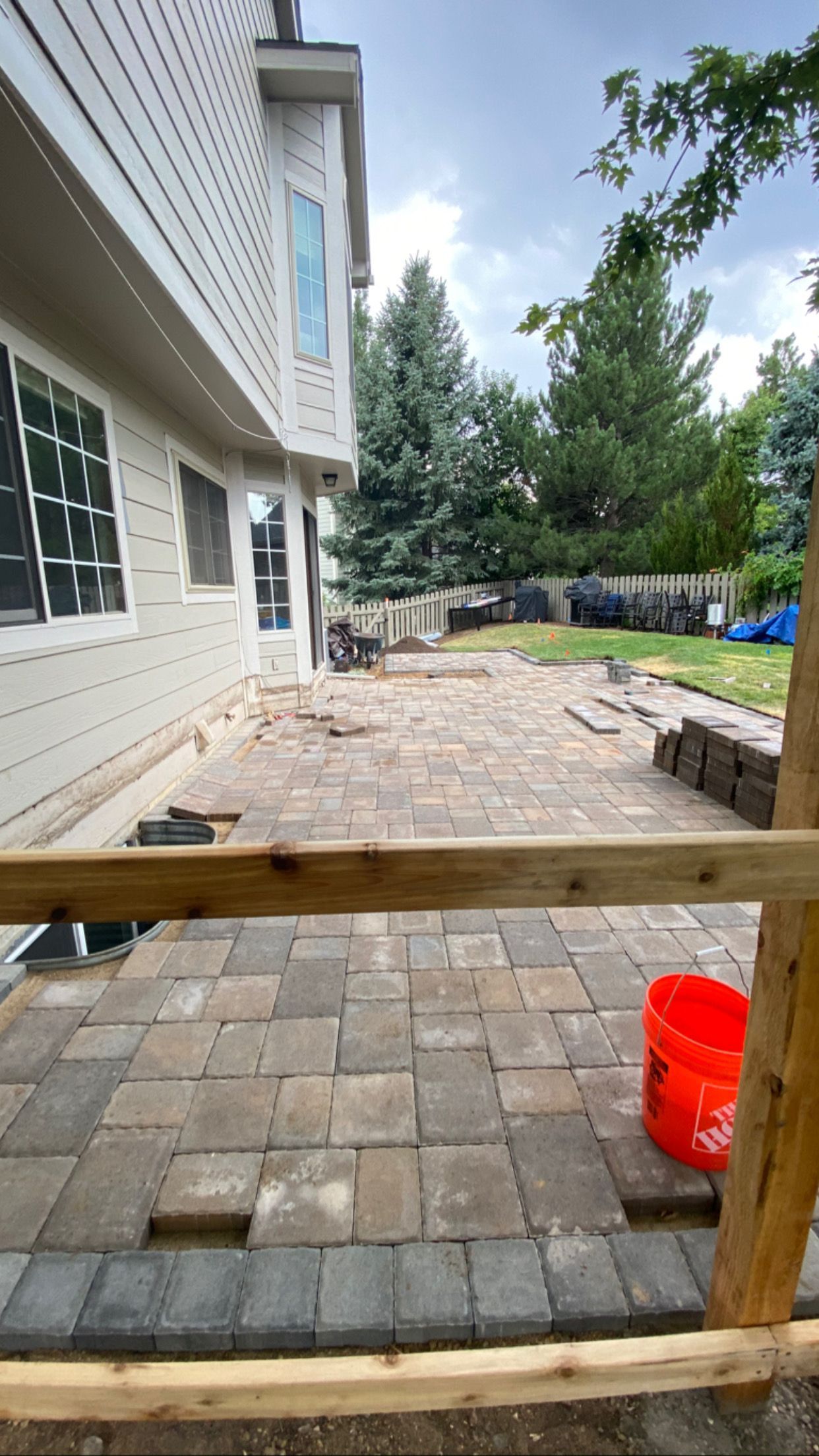Patio being constructed with pavers near a house, with an orange bucket visible.