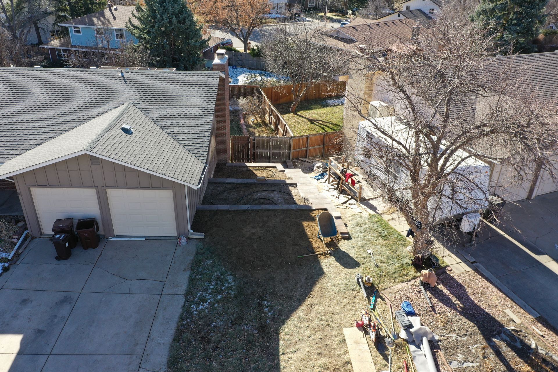 Aerial view of a suburban backyard with a garage, fence, and tree; construction activity in progress.