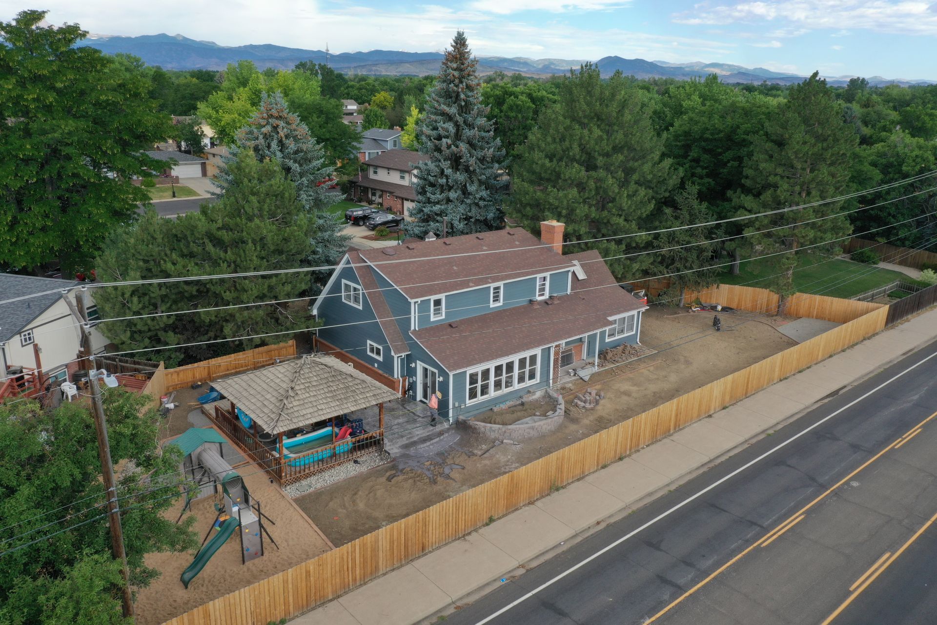 Aerial view of a blue house with a brown roof and a wooden fence along a road.