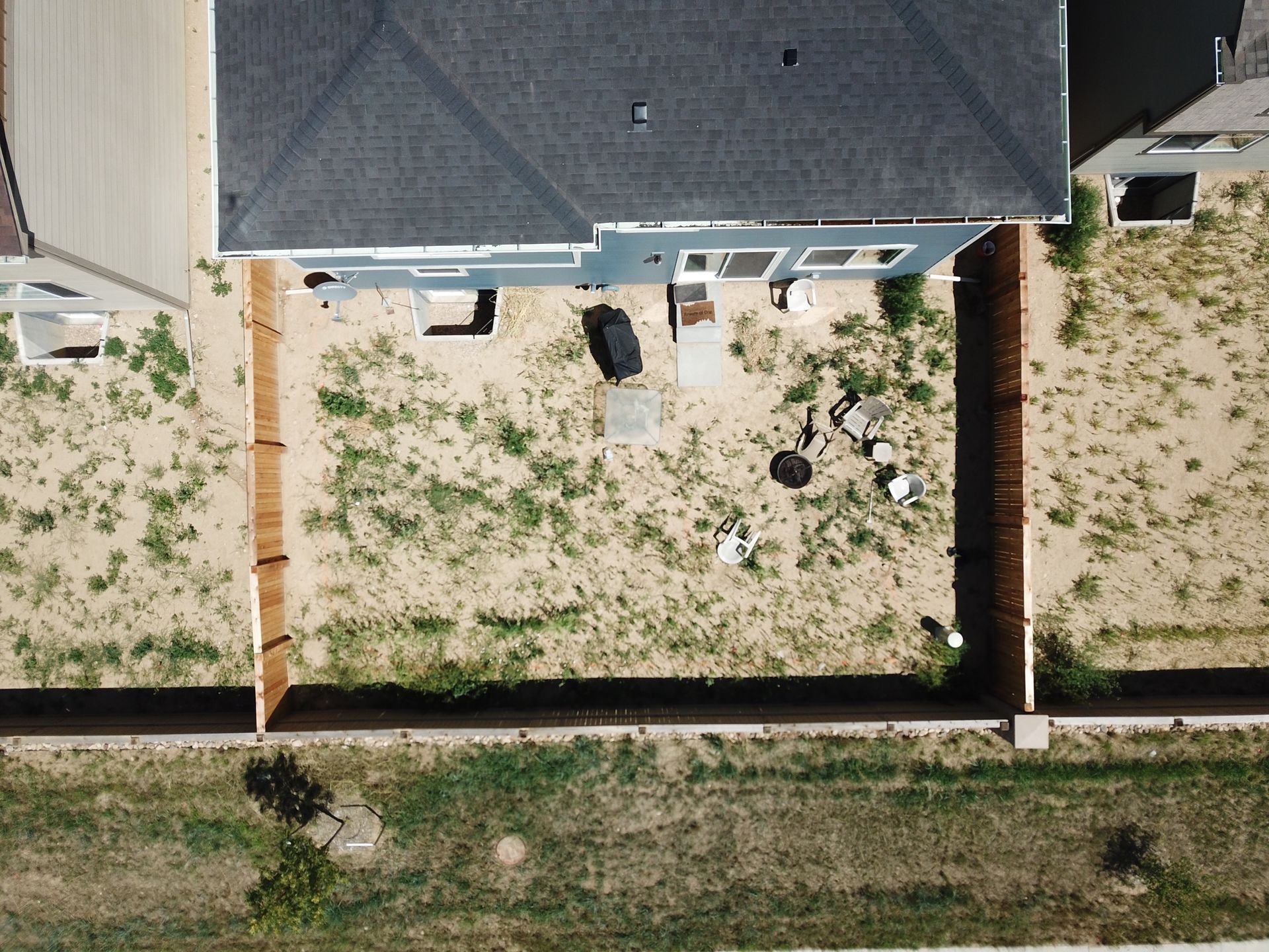 Aerial view of a backyard with a house, fences, and sparse vegetation on dry land.