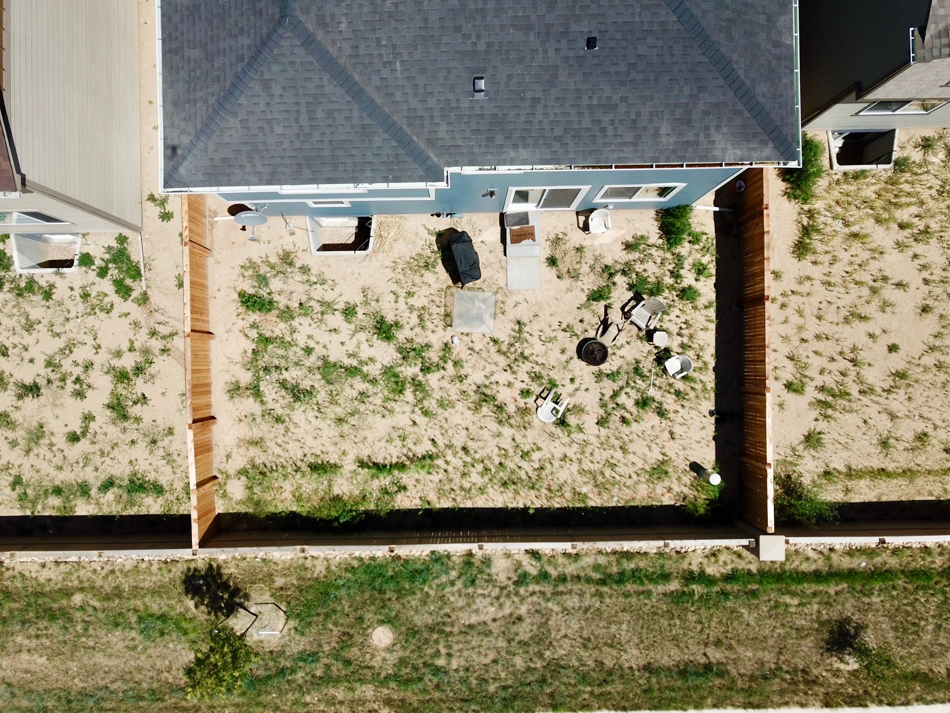 Overhead view of a backyard with a house, wooden fences, and patchy grass.