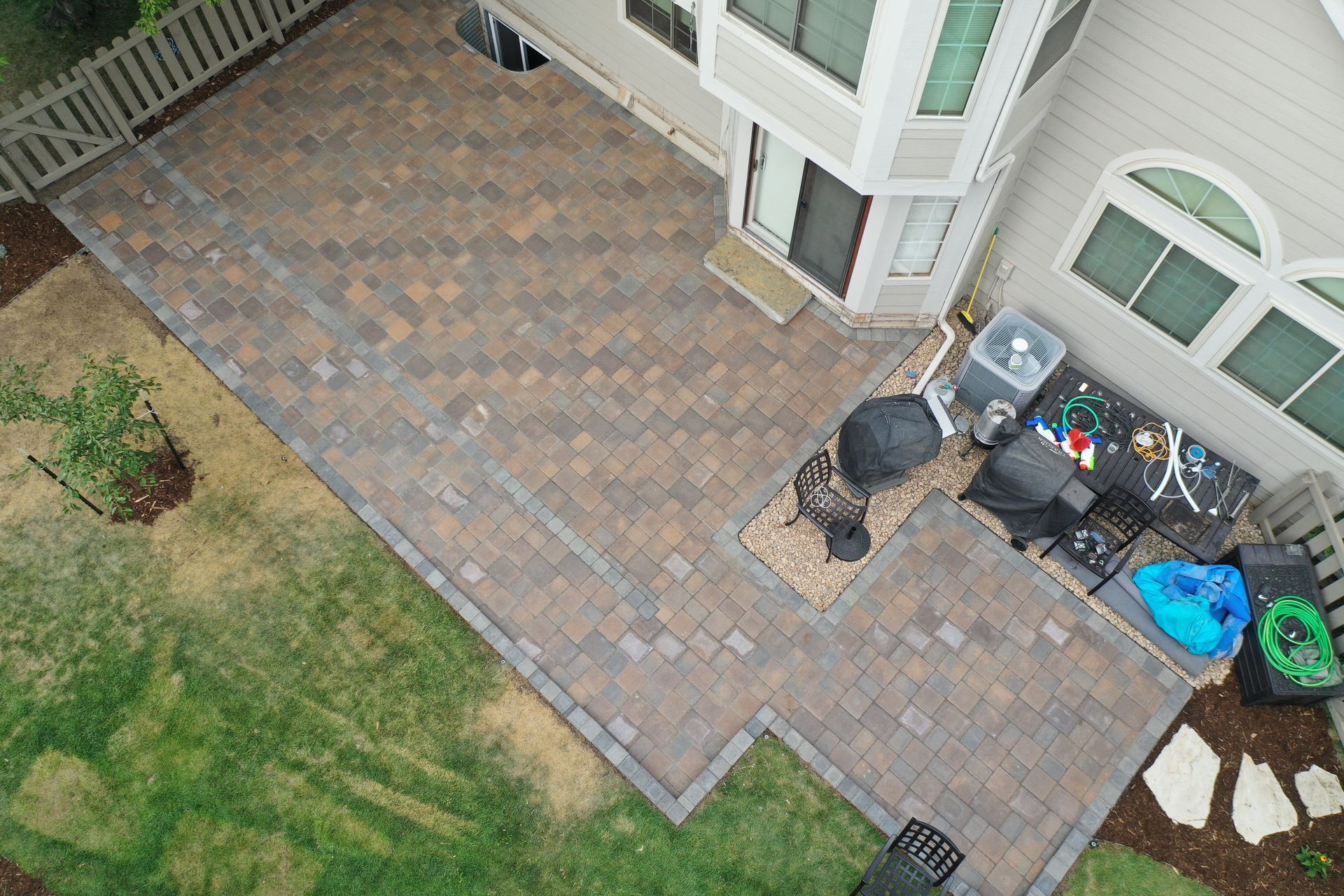 Overhead view of a brick patio with a house, grass, and a white fence.