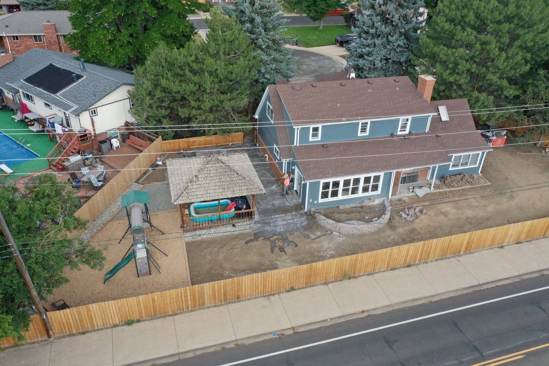 An aerial view of a blue house with a brown roof and a backyard playground and gazebo.