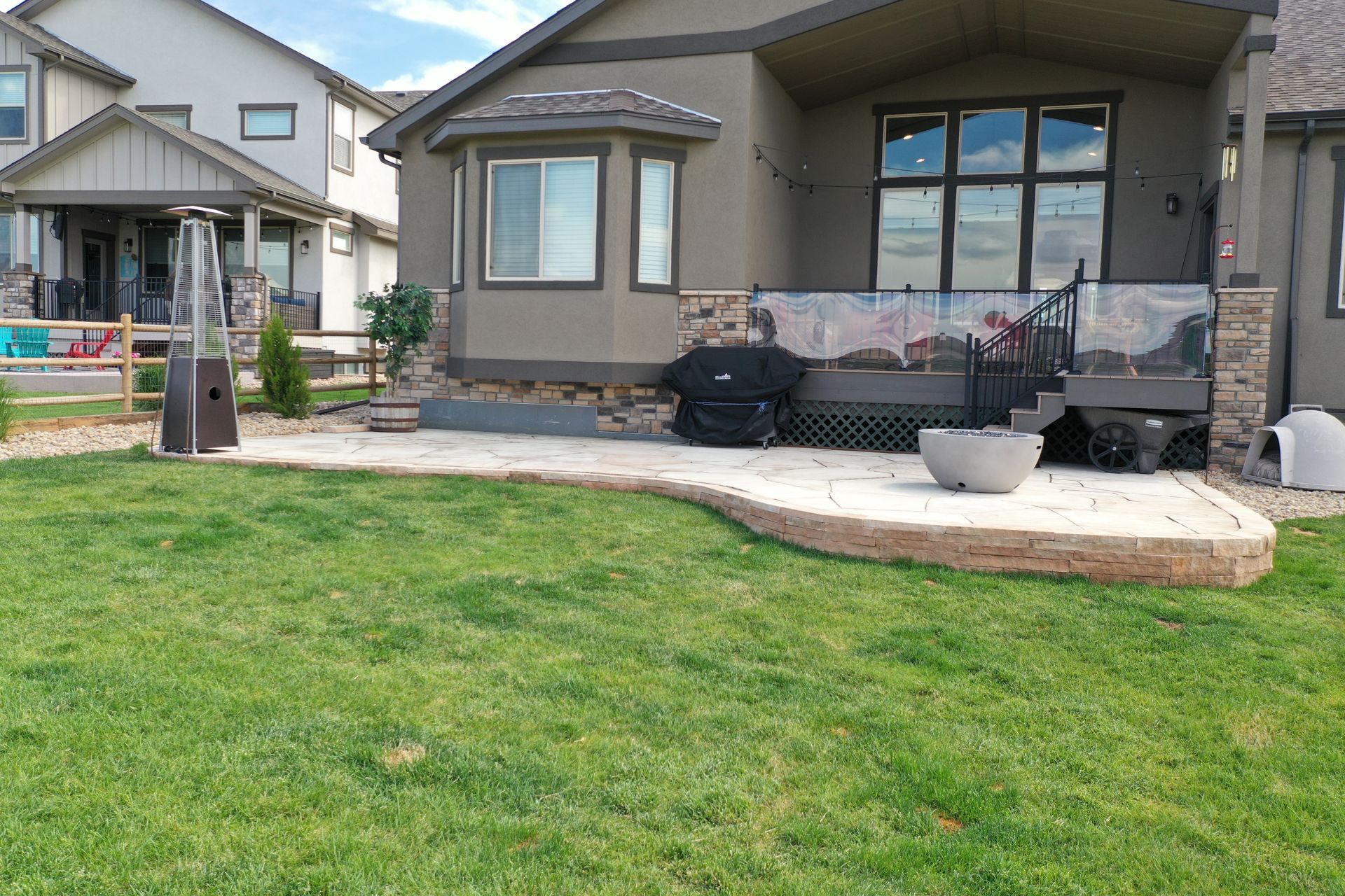 Backyard patio with lawn, retaining wall, grill, and house.