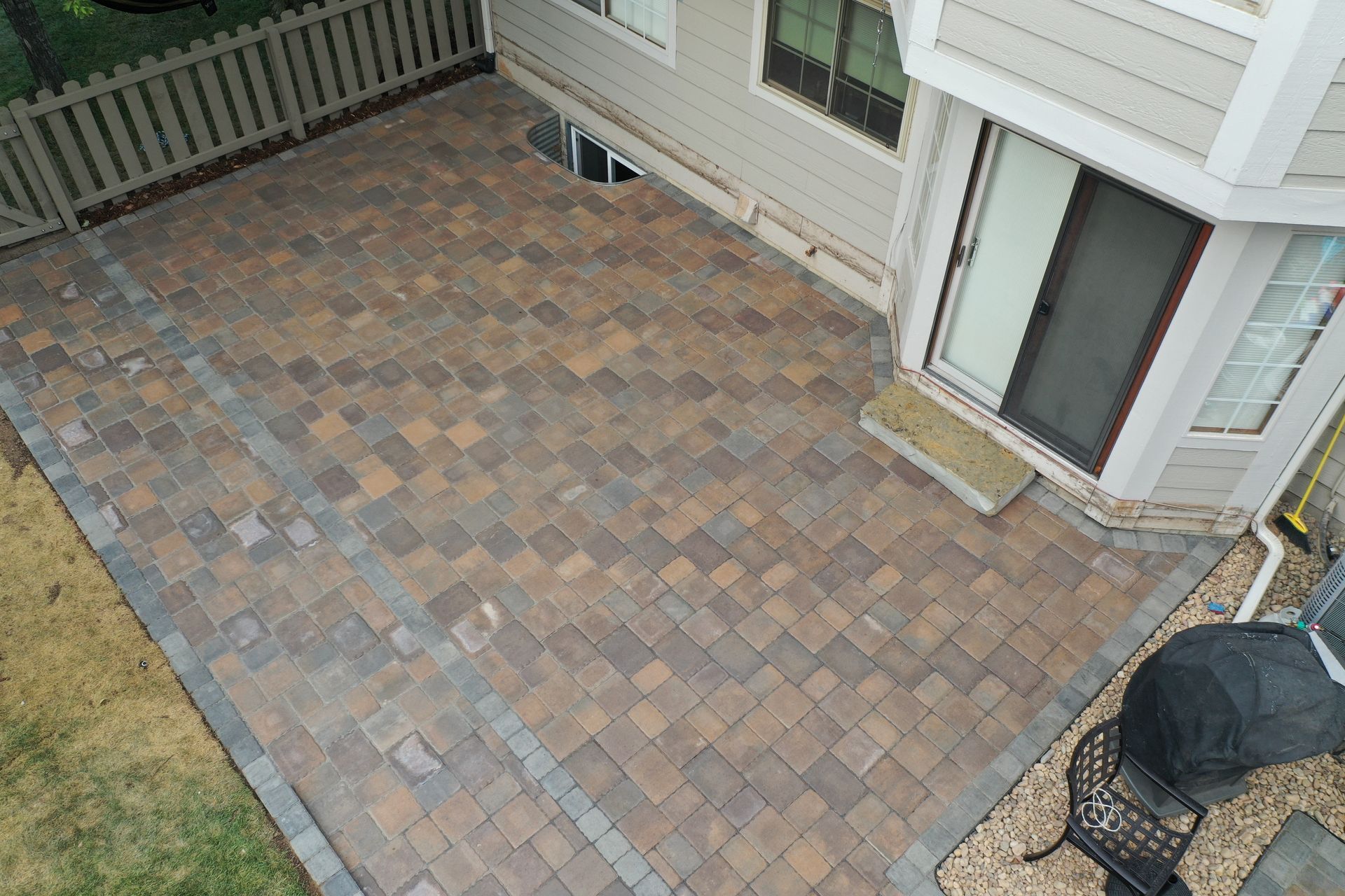 Overhead view of a brick patio next to a house, with a grill and grass visible.