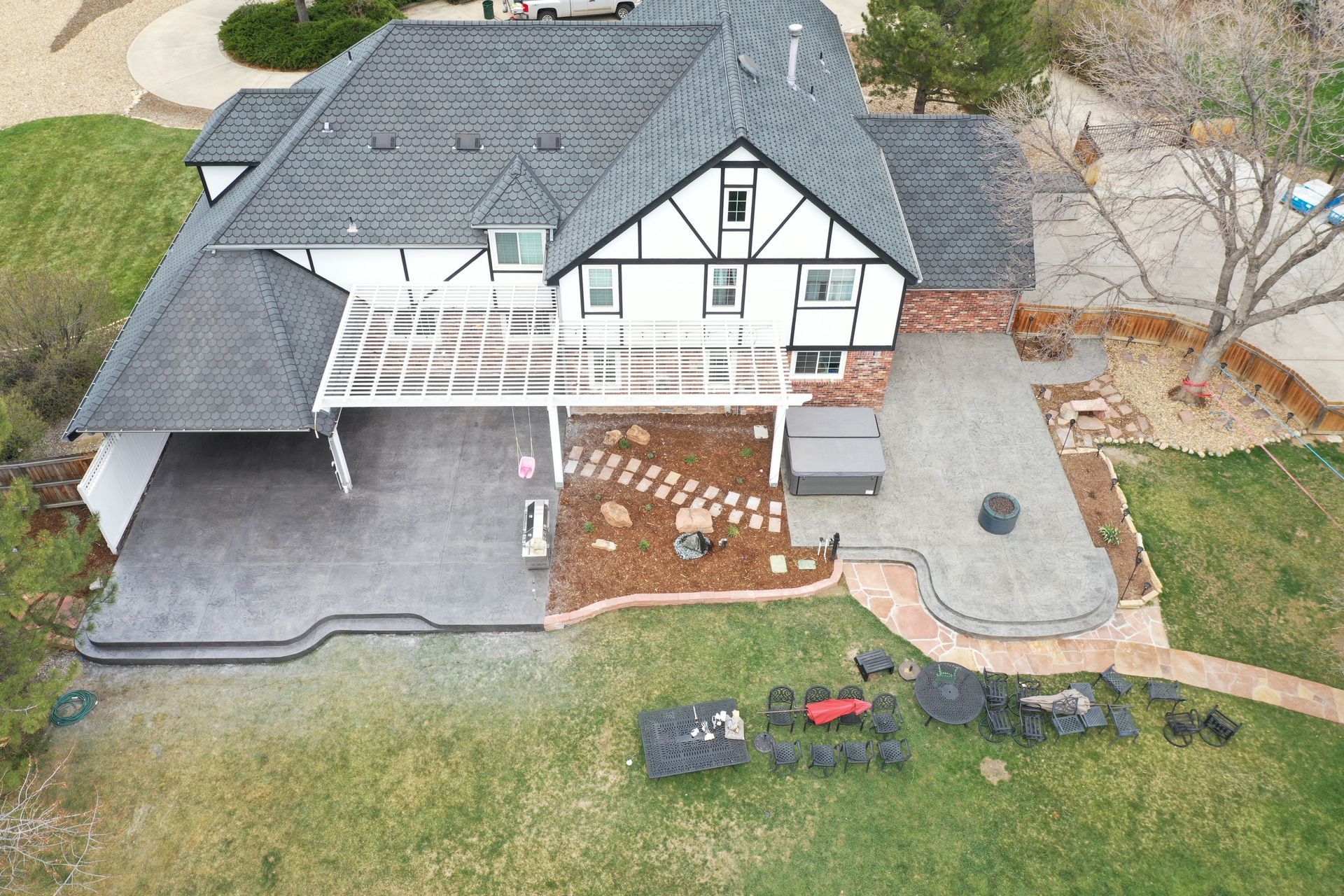Aerial view of a Tudor-style house with a patio, covered carport, and extensive landscaping.