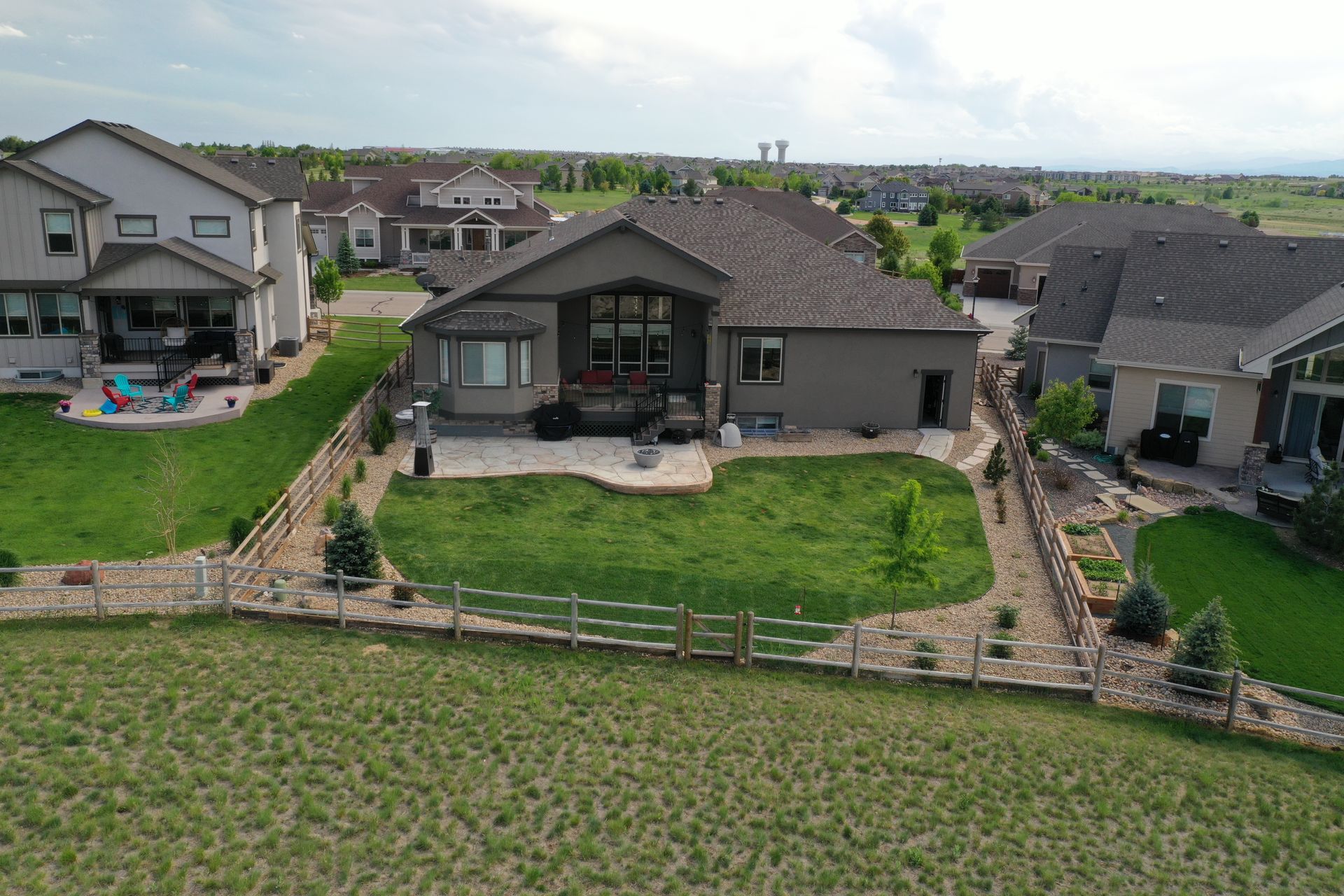 Aerial view of a gray house with a stone patio, grassy lawn, and wooden fence.