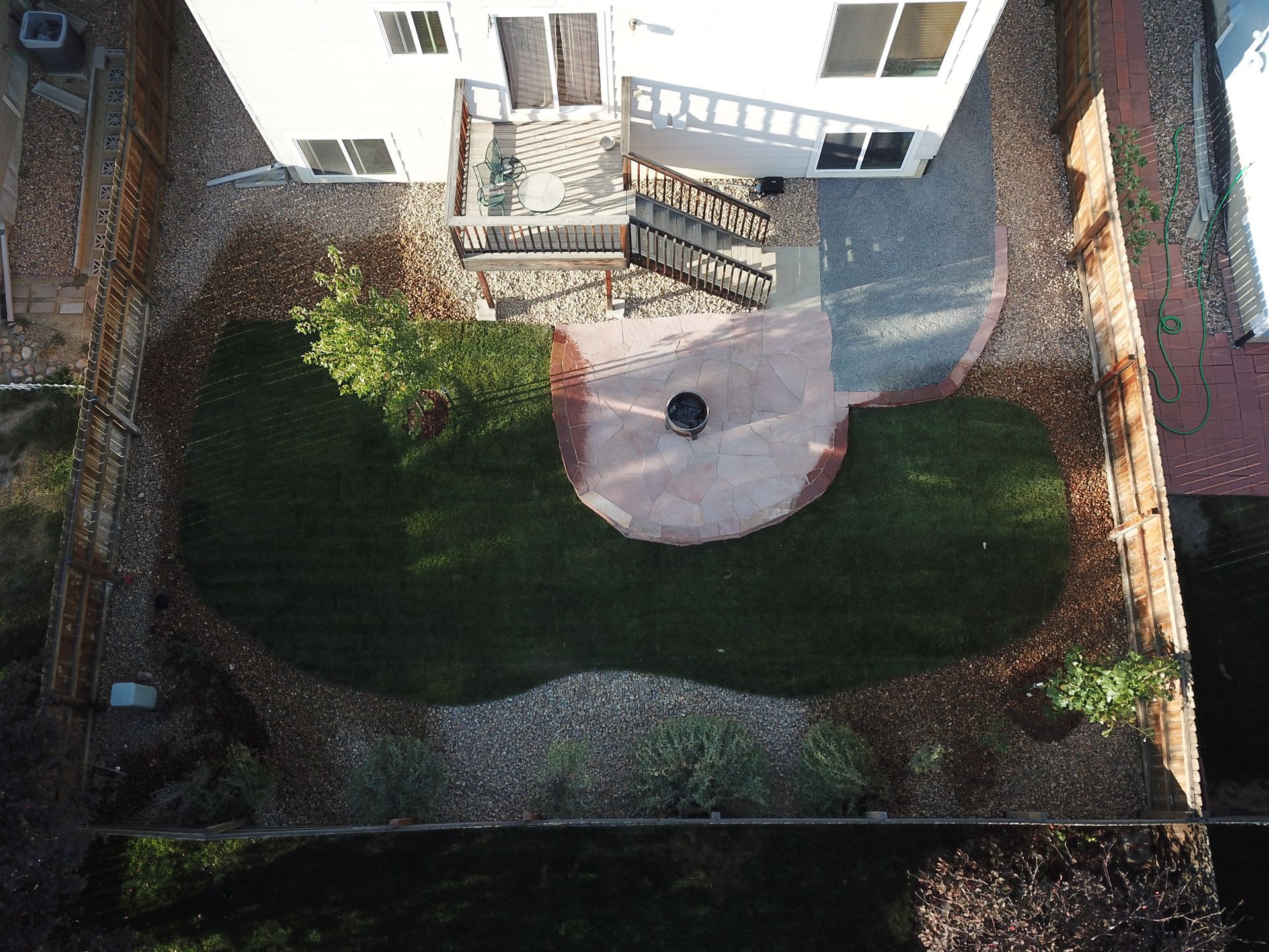 Overhead view of a backyard with a curved brick patio, green lawn, and two-story white house.