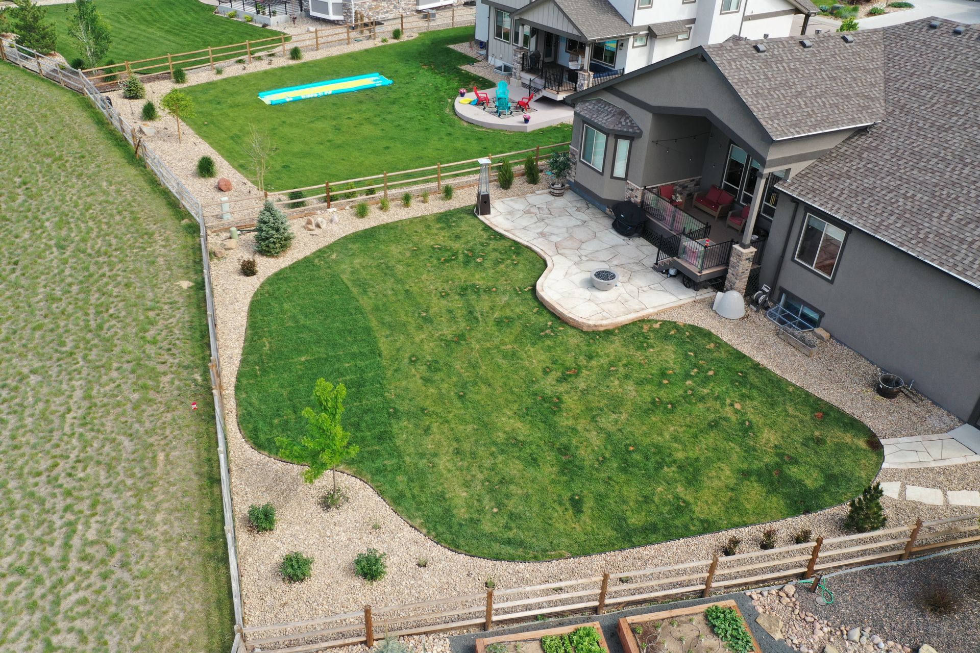 Aerial view of a suburban backyard with a manicured lawn, stone patio, and wooden fence.