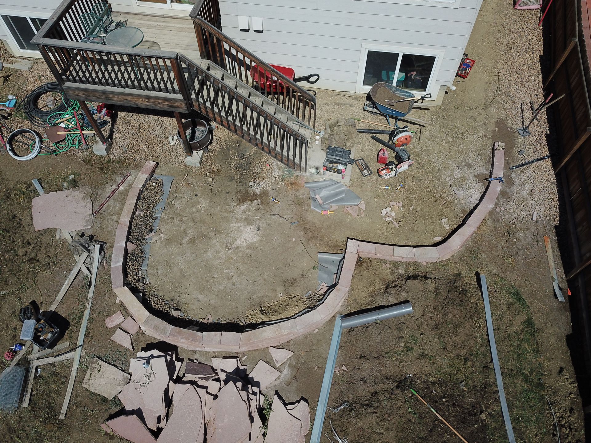 Overhead view of a backyard with a circular brick wall being constructed near a wooden deck.