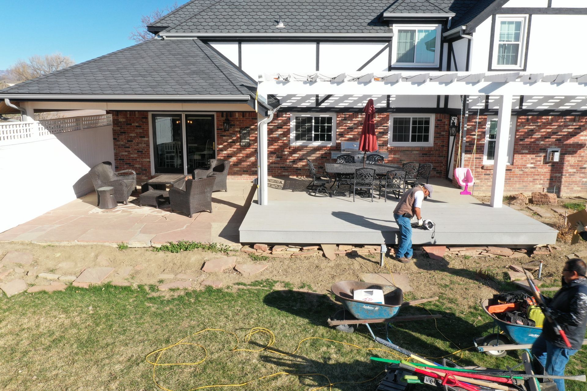 Men working on a patio construction next to a house with an attached pergola and outdoor furniture.