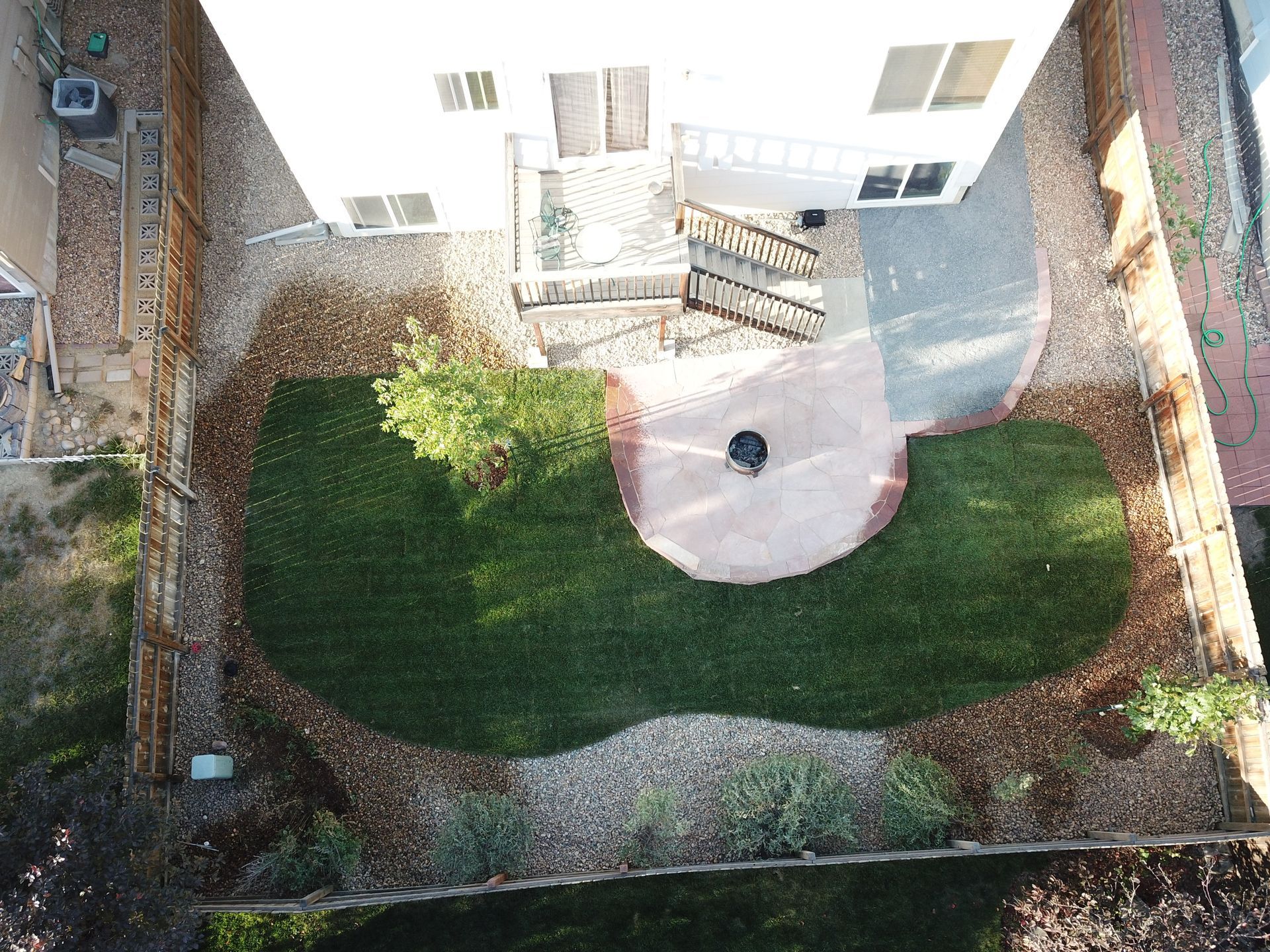 Overhead view of a backyard with a patio, lawn, and gravel, with a two-story beige house.