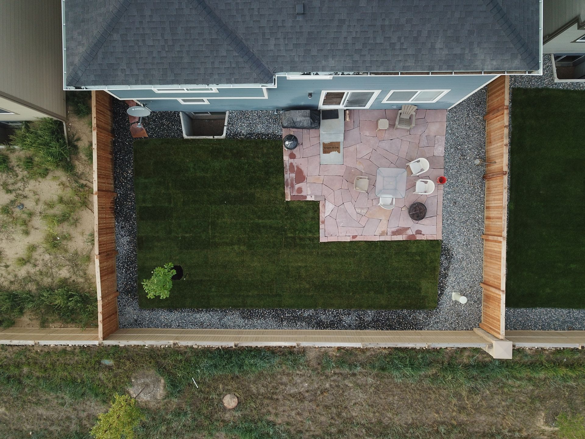 Overhead view of a backyard with patio, grass, gravel borders, and wooden fences.