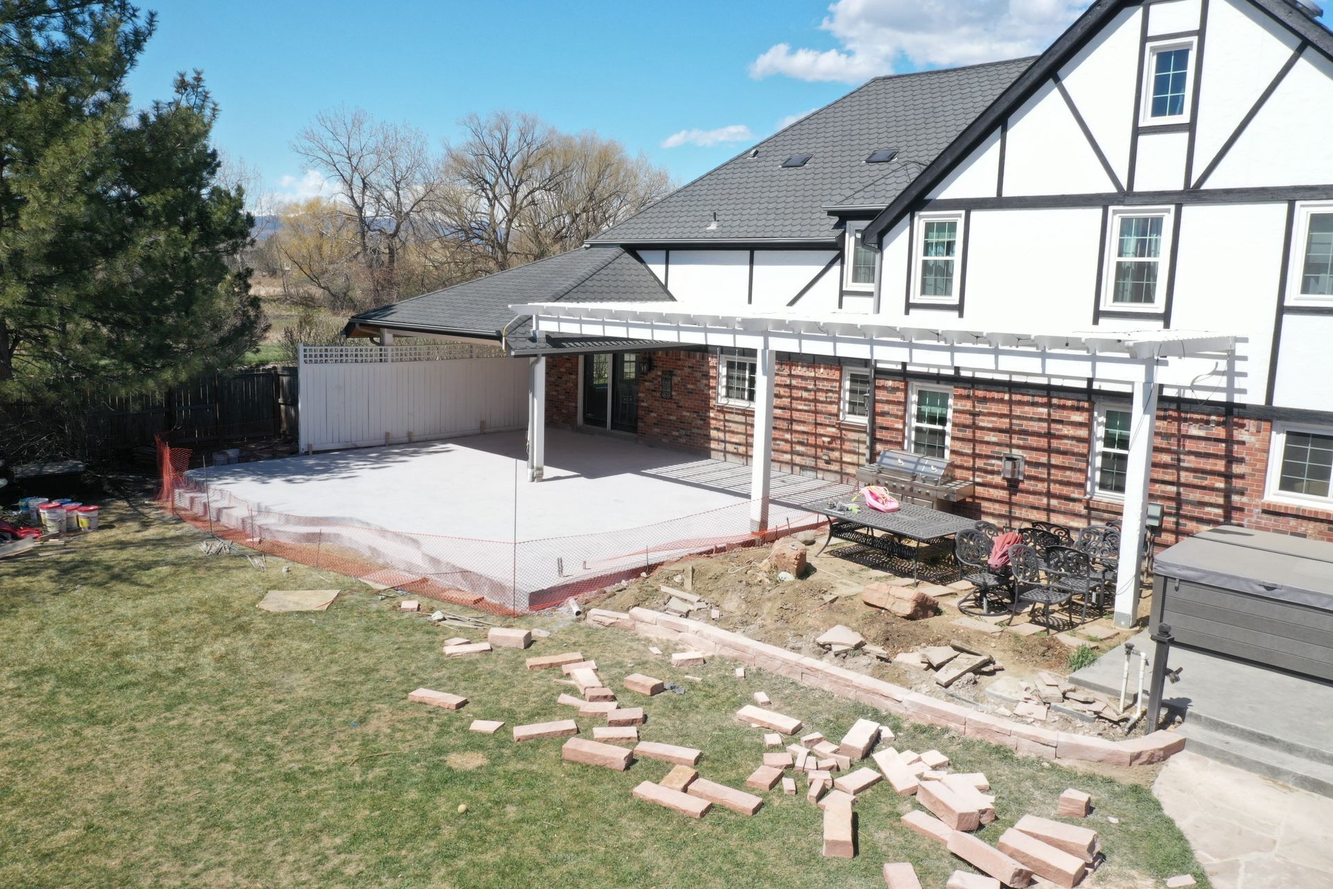 Backyard renovation: demolished brick patio with a partial pergola, adjacent to a two-story Tudor-style house.
