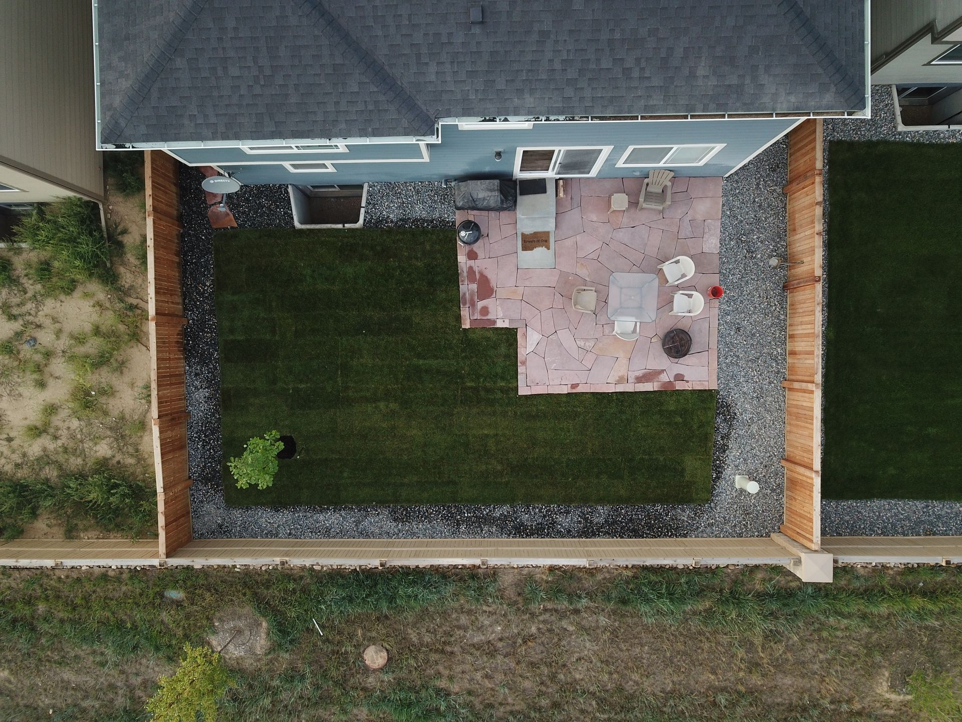 Overhead view of a backyard with a grass lawn, patio, and wooden fence, with a house in the background.