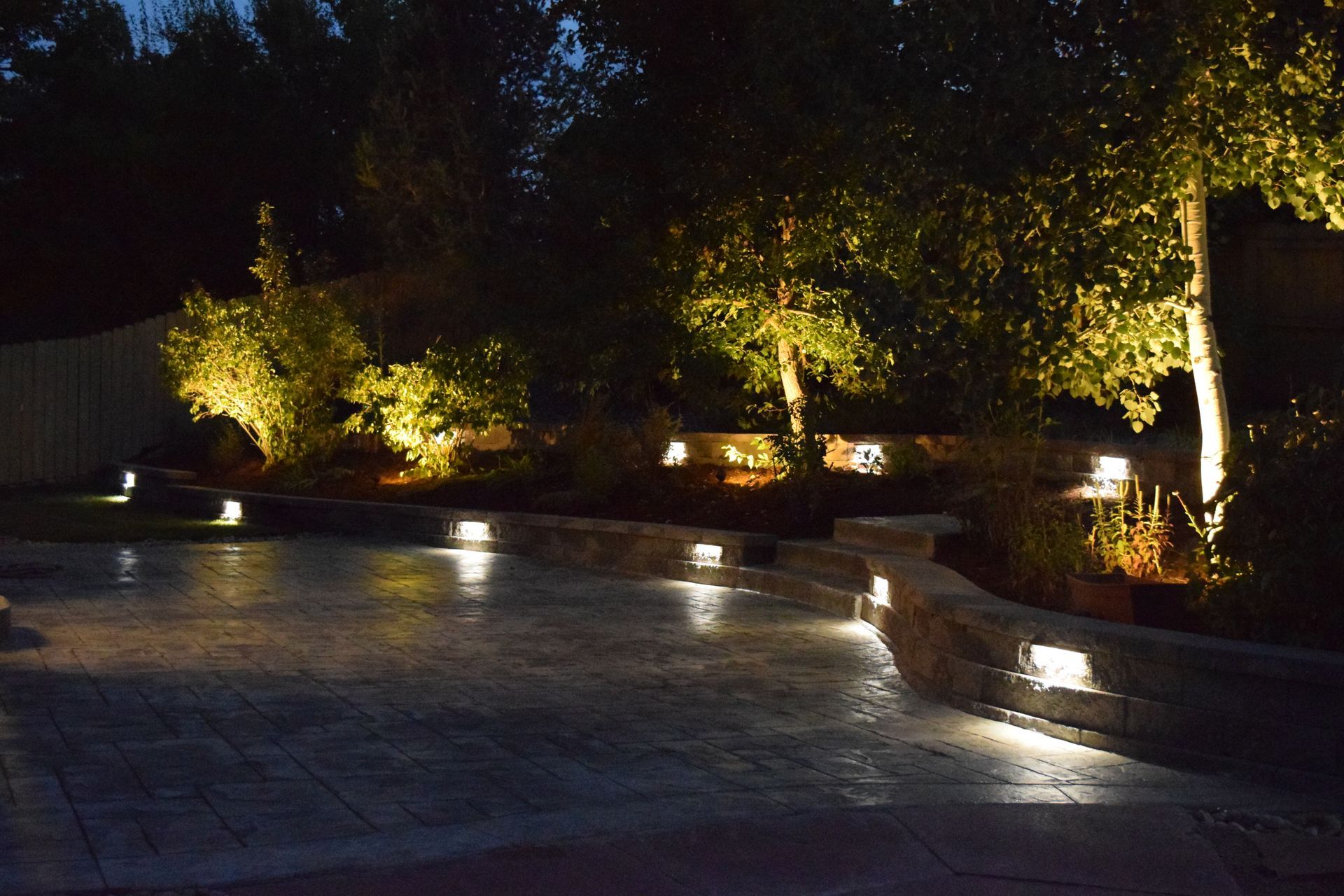 Nighttime illuminated patio with built-in lights, rock wall, and trees, creating a warm ambiance.