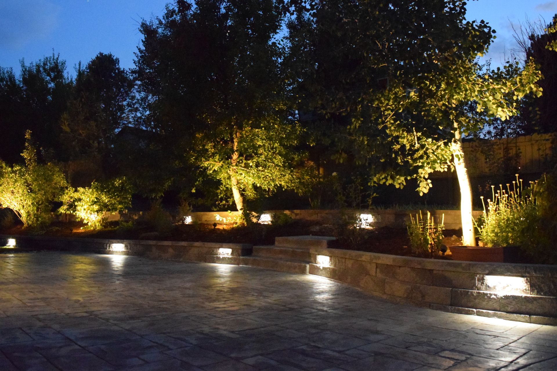 Nighttime outdoor scene with lit trees, stone walls, and square ground lights.