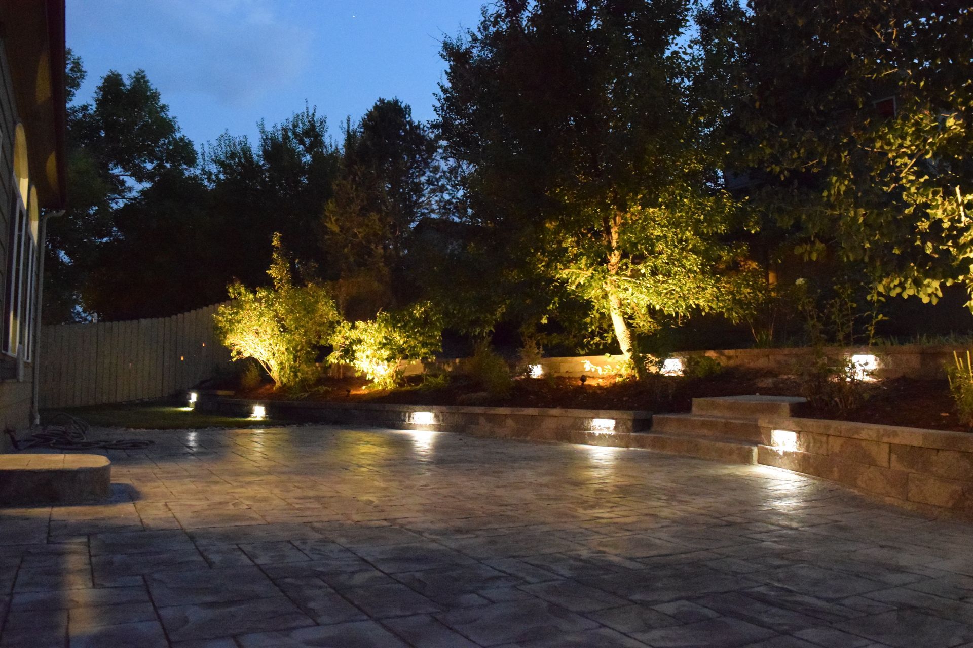 Night scene: illuminated patio with built-in lights, stonework, and trees with up-lighting.