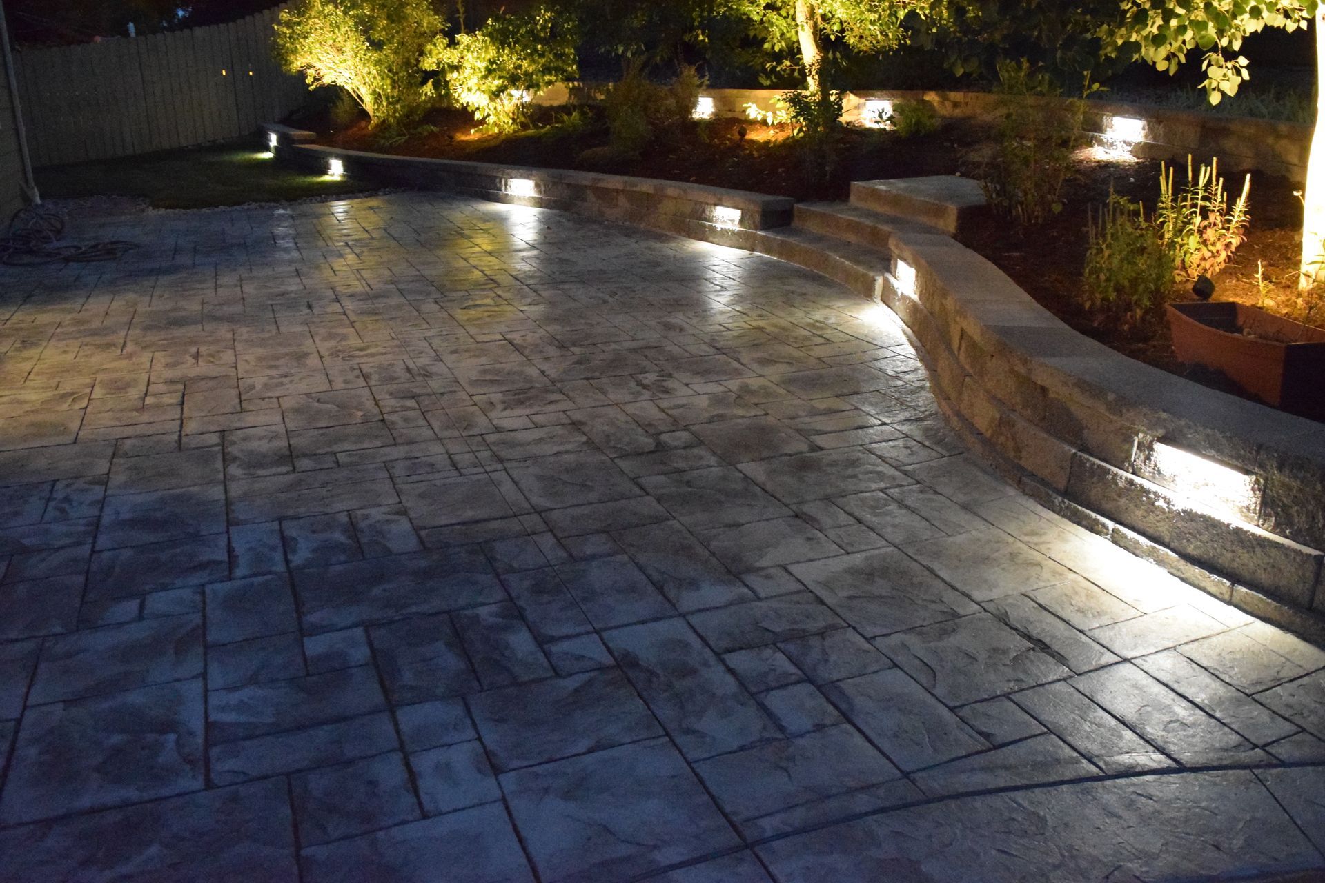 Lit patio with stone retaining wall and path at night.