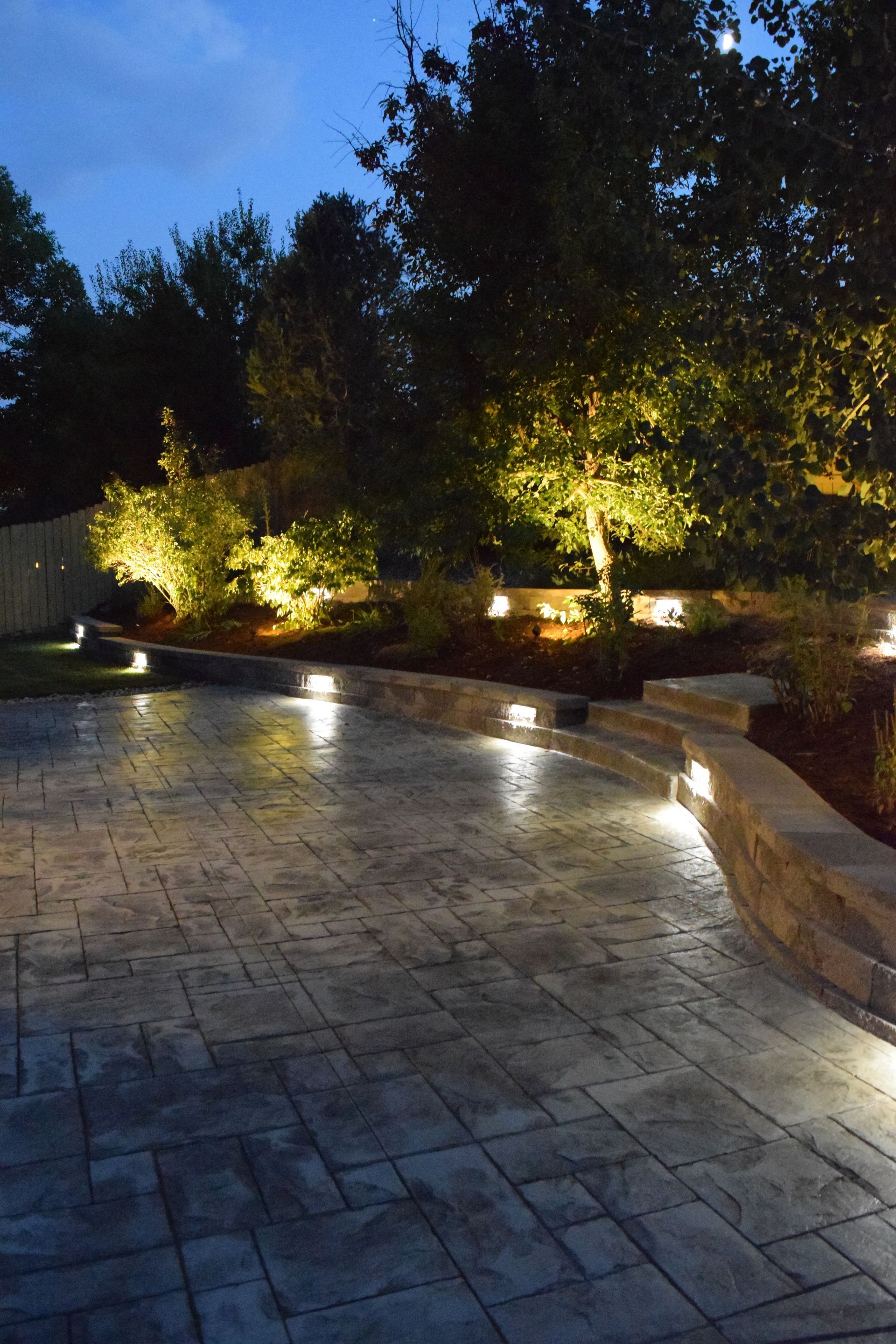 Nighttime outdoor patio with built-in lights, stonework, and illuminated trees.