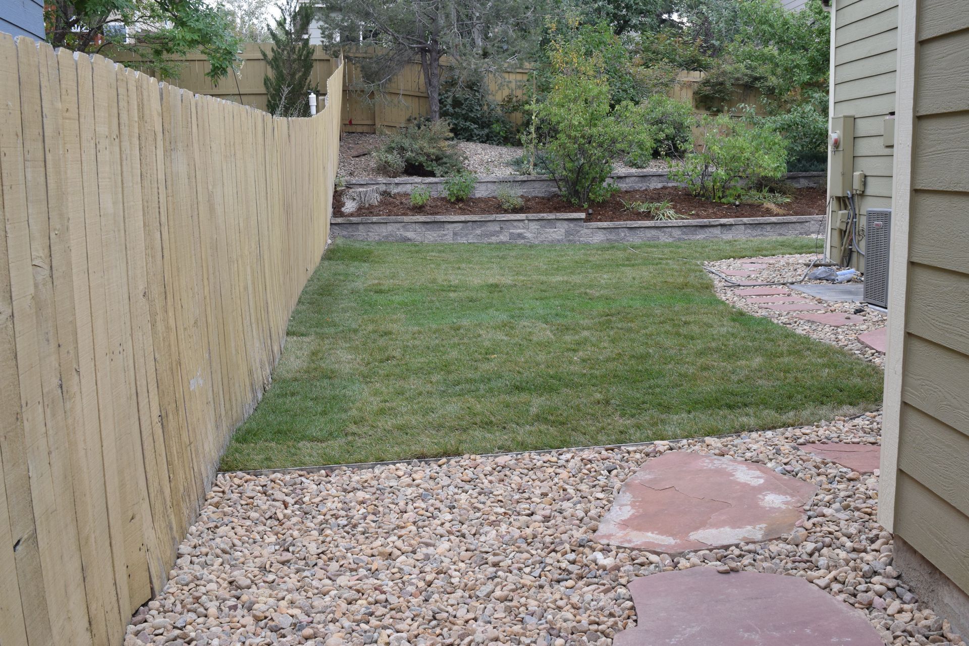 Backyard with grass, gravel, a fence, and a stone walkway.