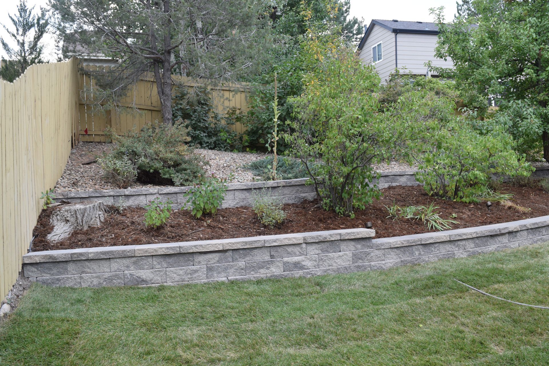 Yard with tiered retaining walls, mulched beds, and a wooden fence.