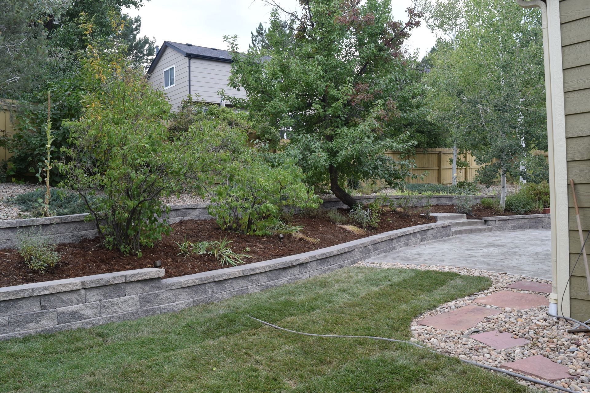 Backyard with retaining walls, greenery, patio, and house in the background.