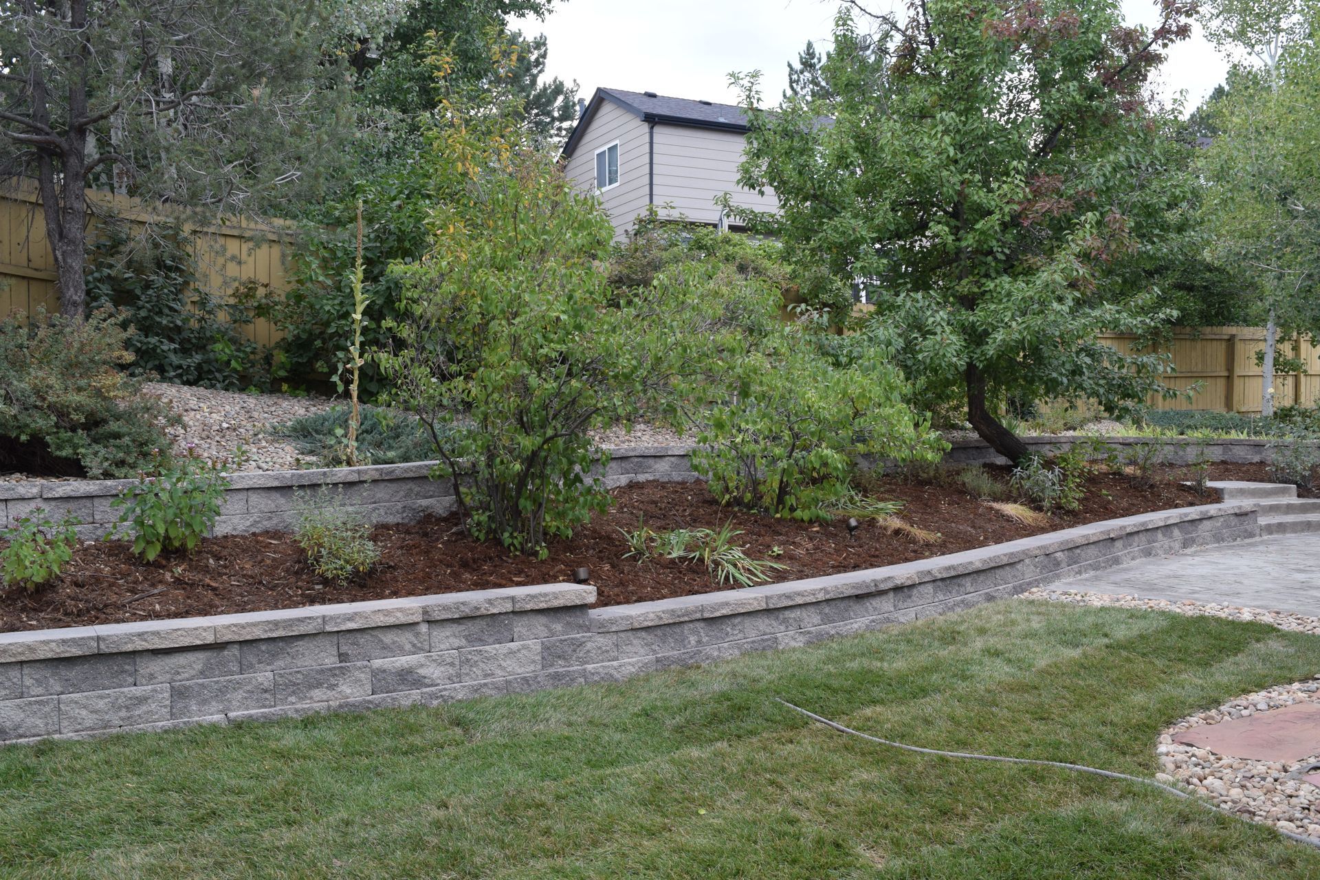 Green lawn with a brick retaining wall and mulched garden bed in front of trees.