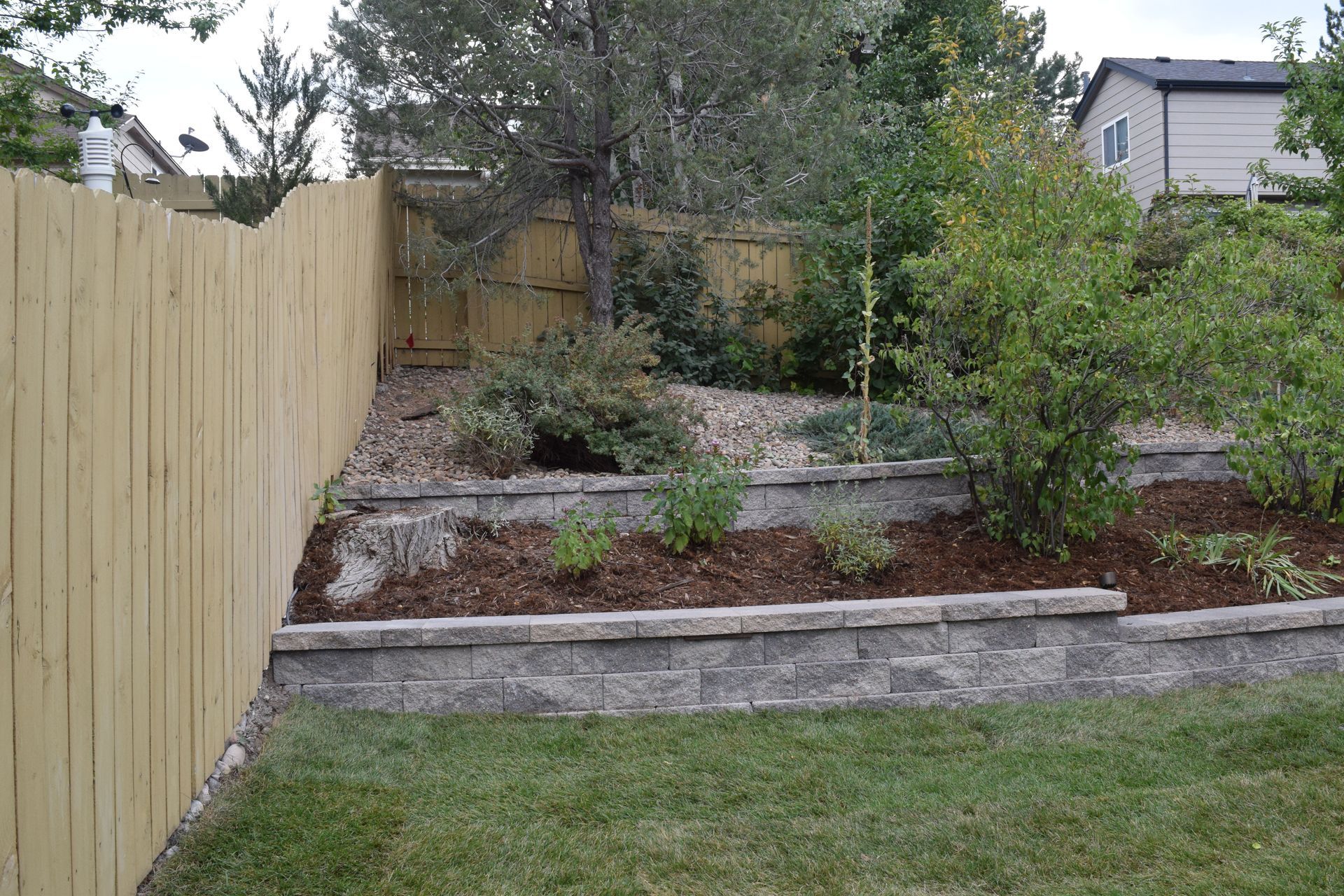 A backyard with a tiered garden bed next to a wooden fence and lawn.