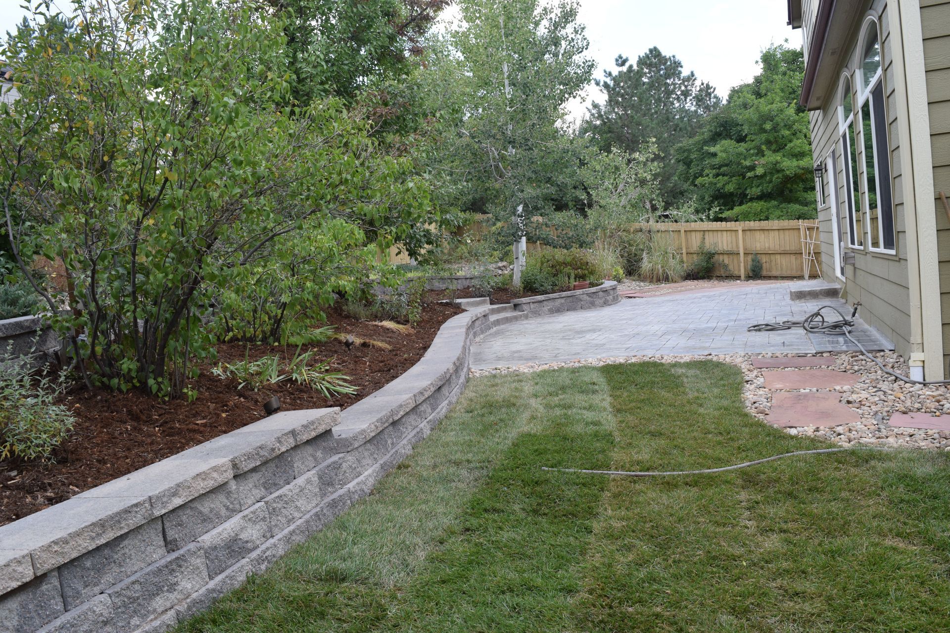 A backyard with a retaining wall, patio, and grass next to a house.