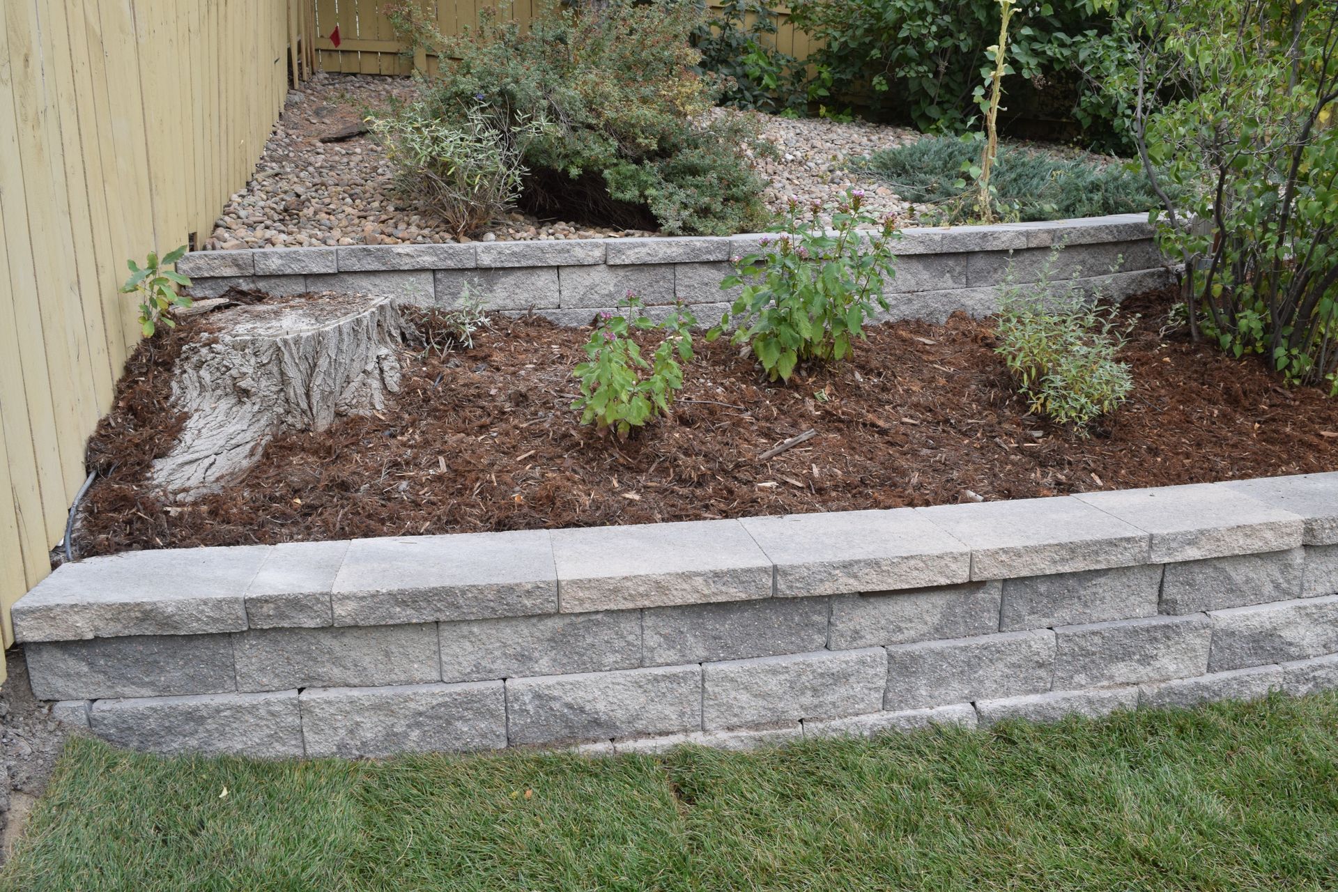 Stone retaining walls with mulch and plants in a backyard.