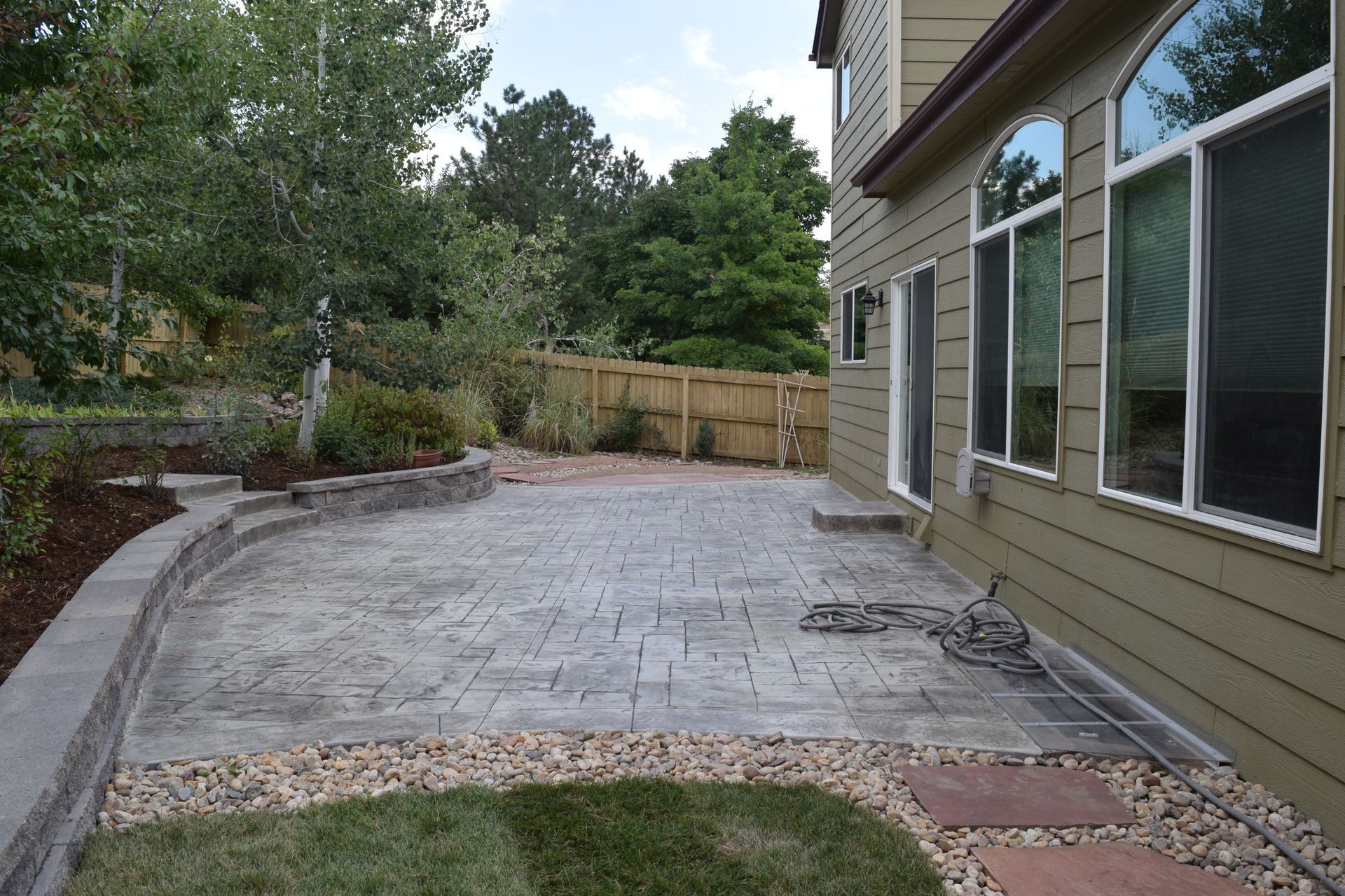 Backyard patio with stamped concrete, a retaining wall, and house with arched windows.