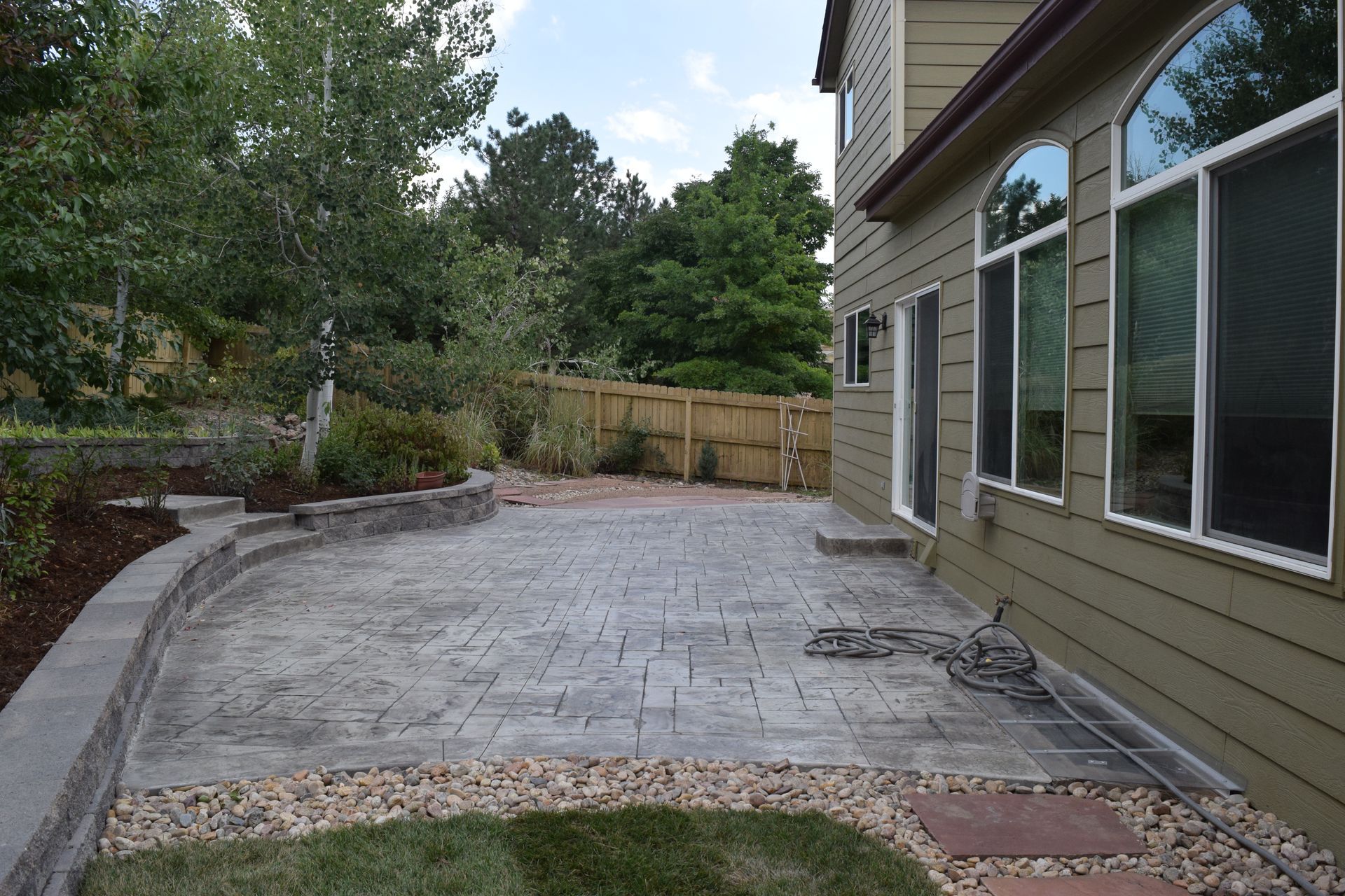 Backyard patio with stone pavers, landscaping, and house with large windows.