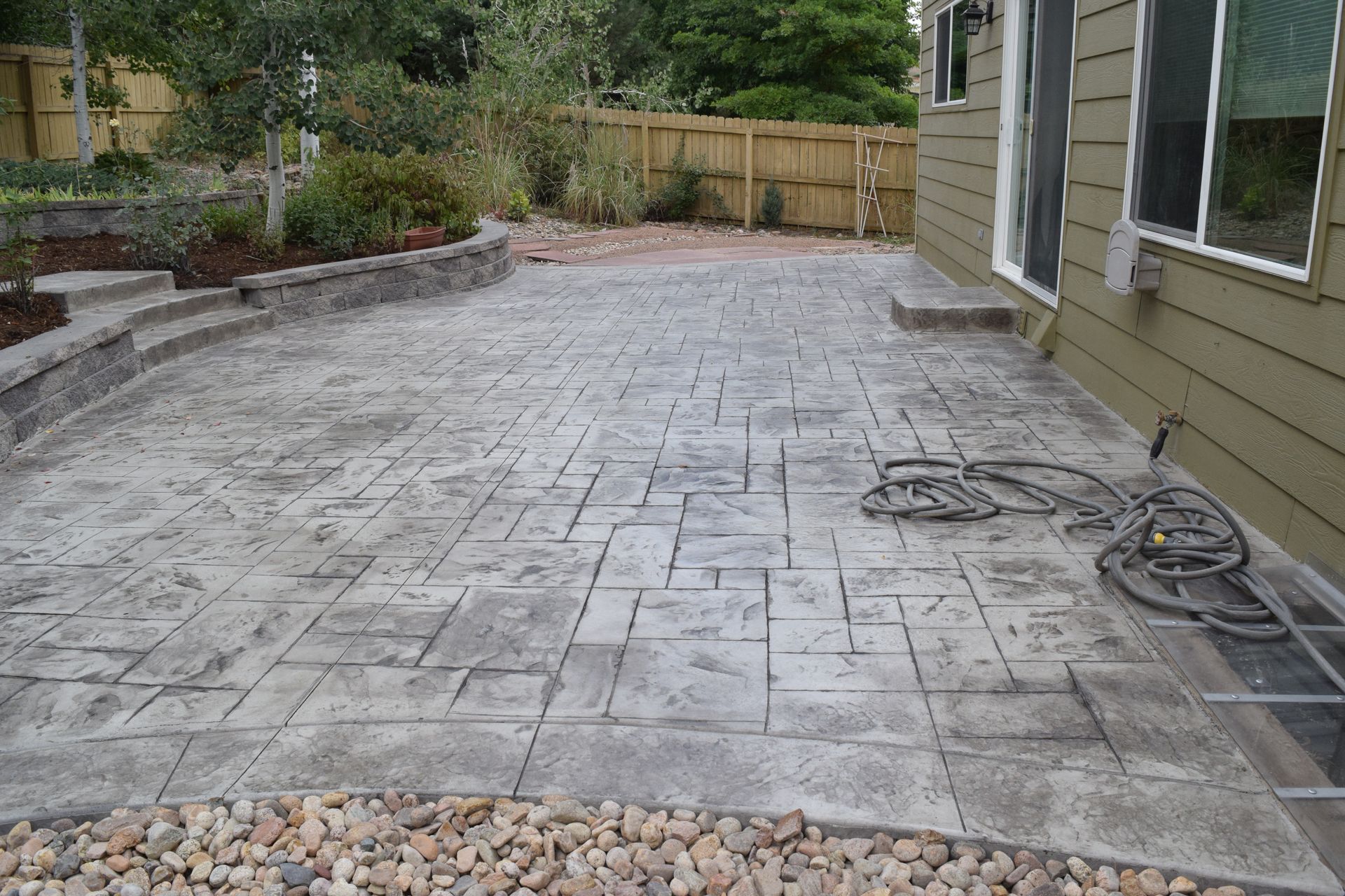 Stamped concrete patio with a stone border next to a house, edged with river rocks.
