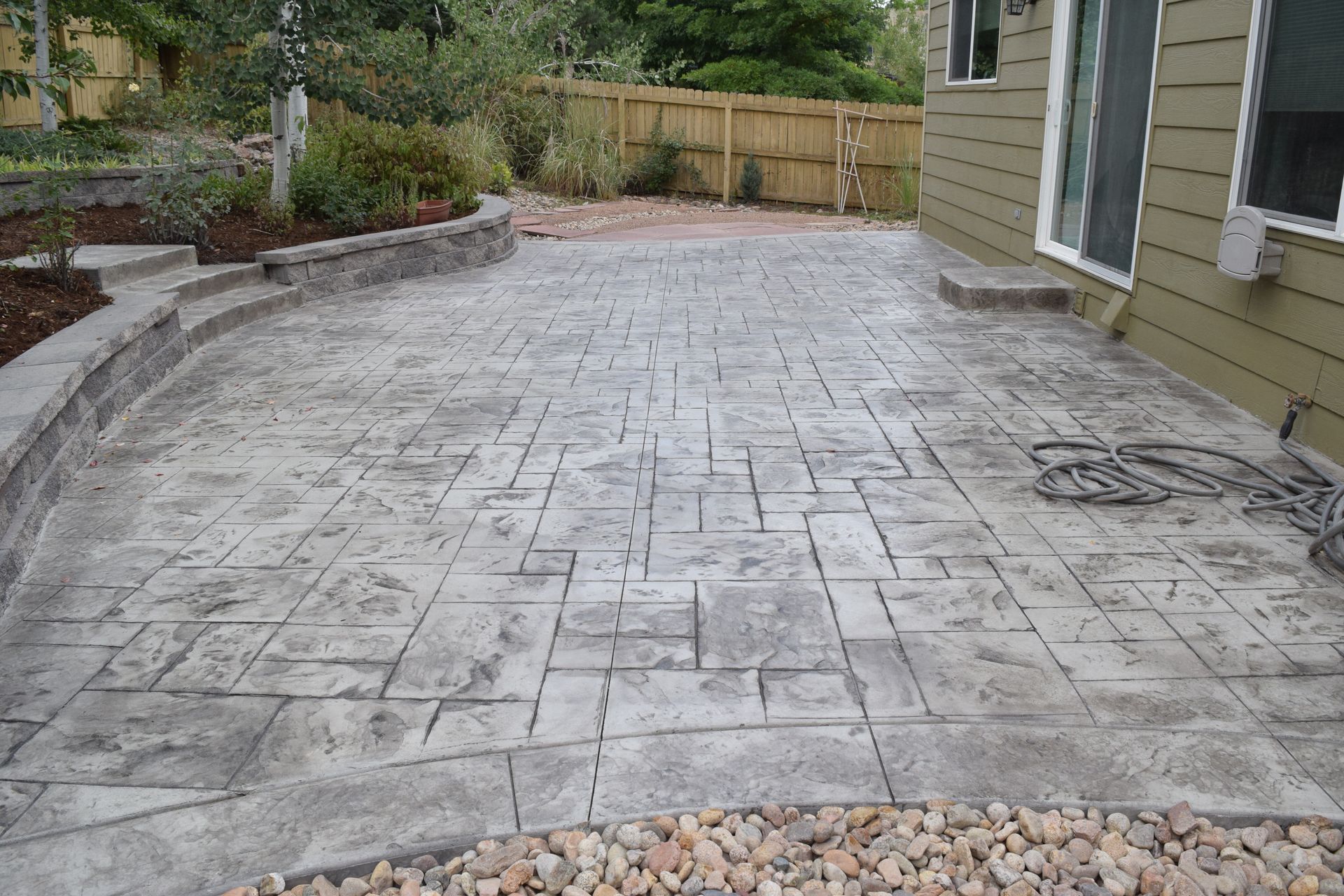 Stamped concrete patio with a textured pattern and a gravel border next to a beige house.
