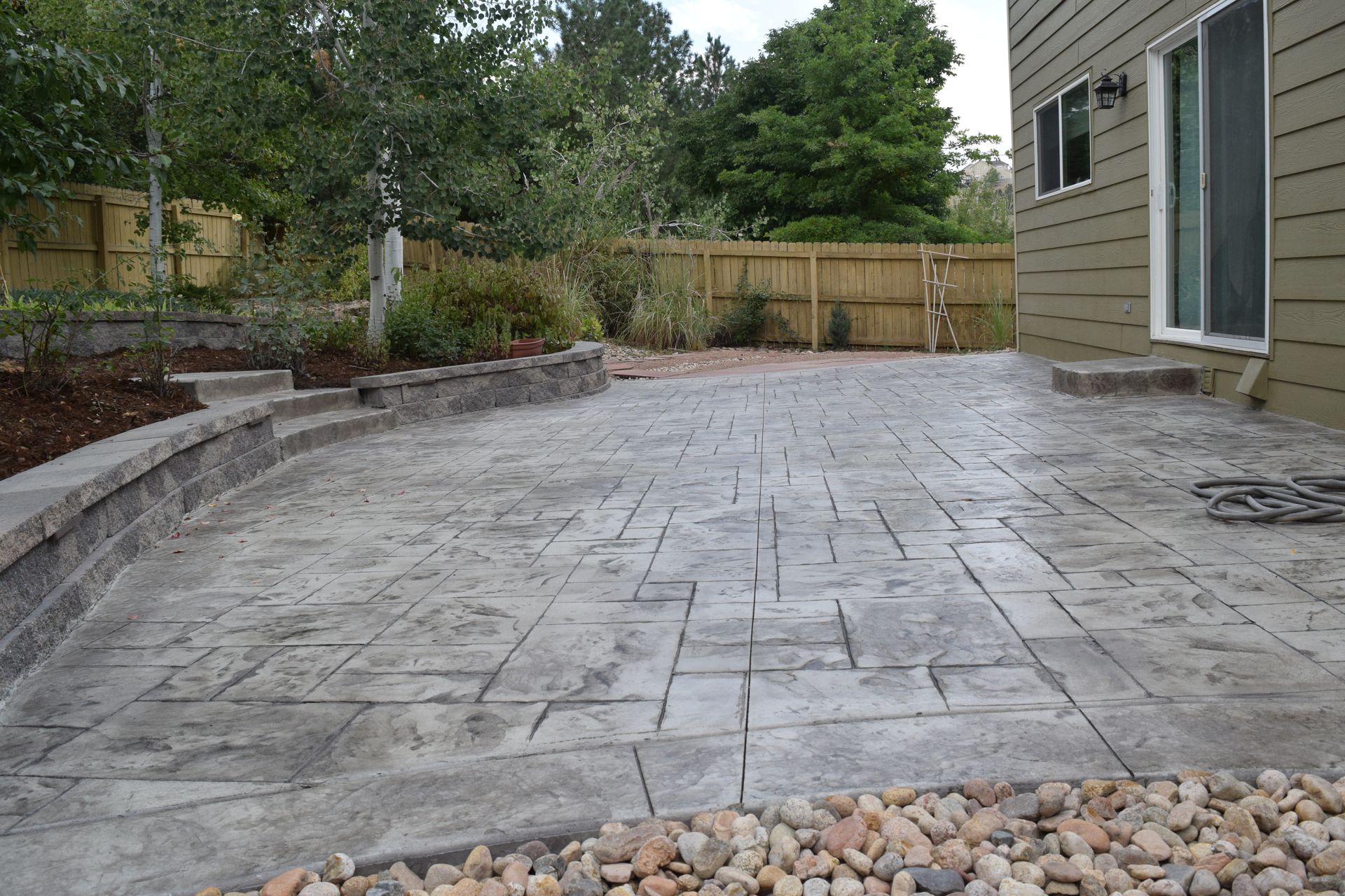 Concrete patio with textured surface, bordered by low wall, house, and fence.