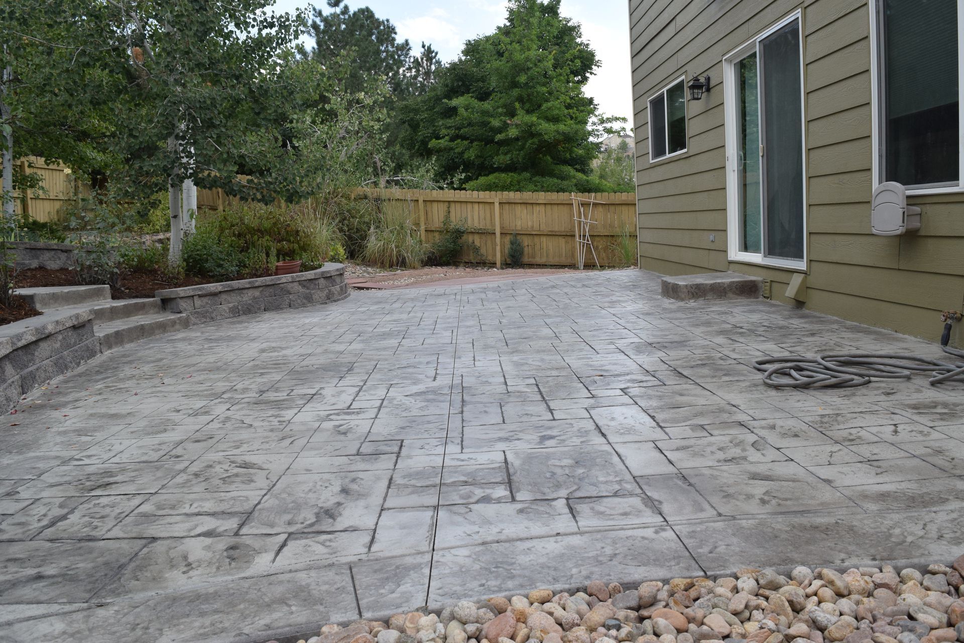 Concrete patio with a patterned design, next to a house and garden area.