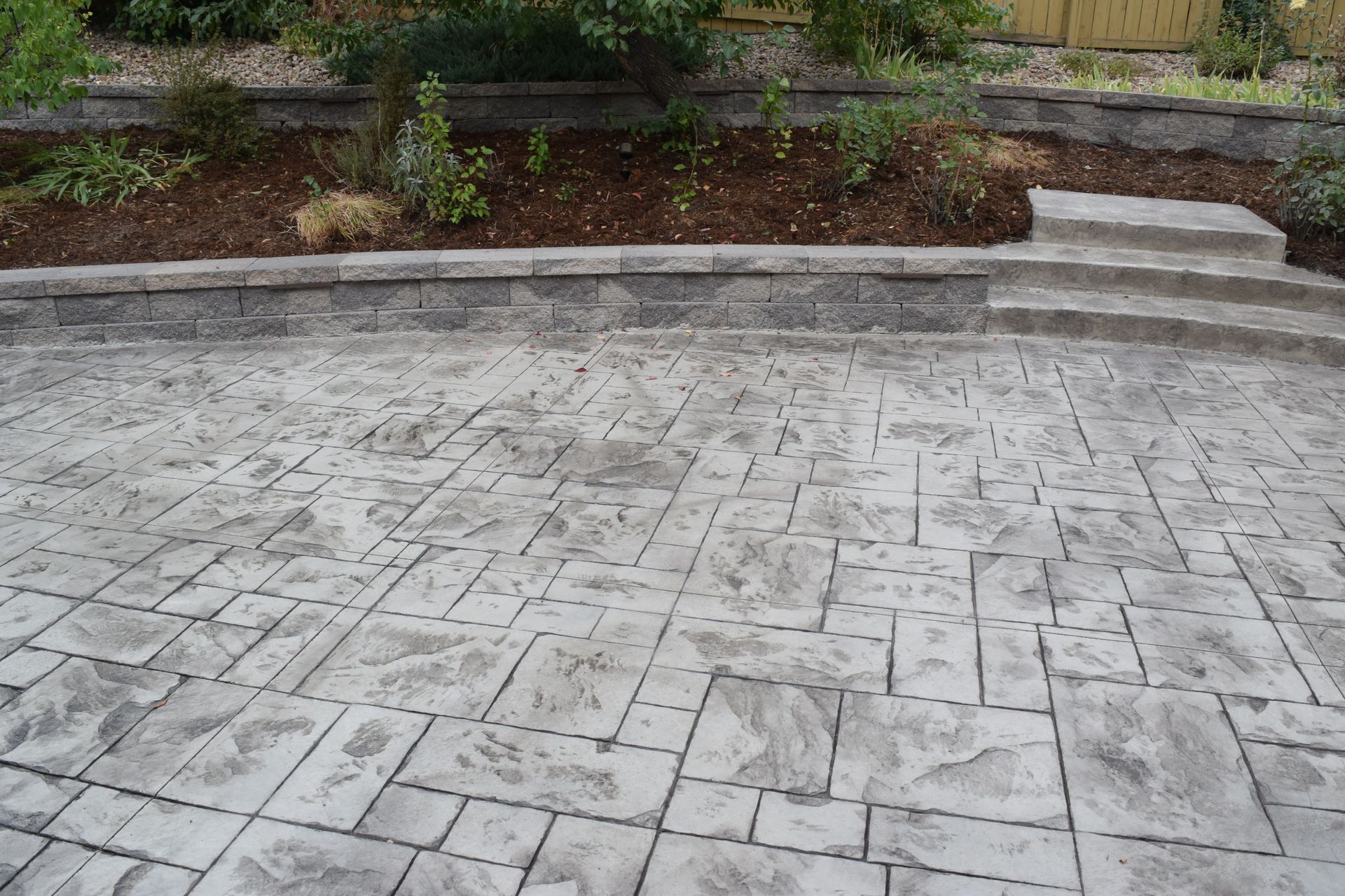 Stamped concrete patio with steps and a retaining wall, bordered by a garden.