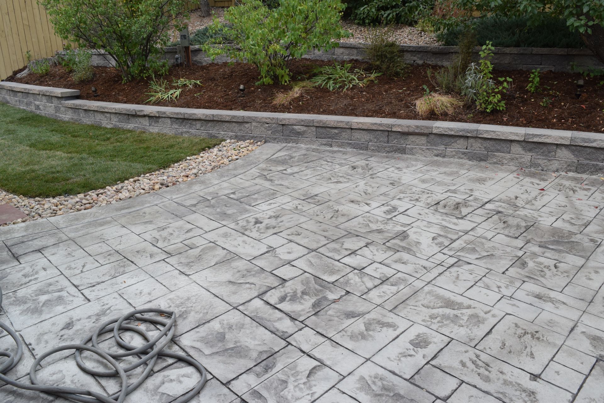 Concrete patio with a stamped stone pattern, beside a grassy area and a garden.