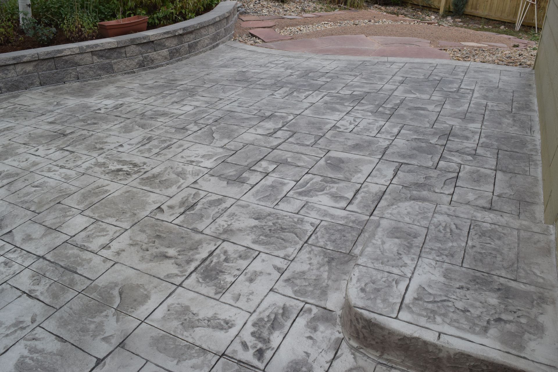 Textured gray concrete patio with a retaining wall and garden.