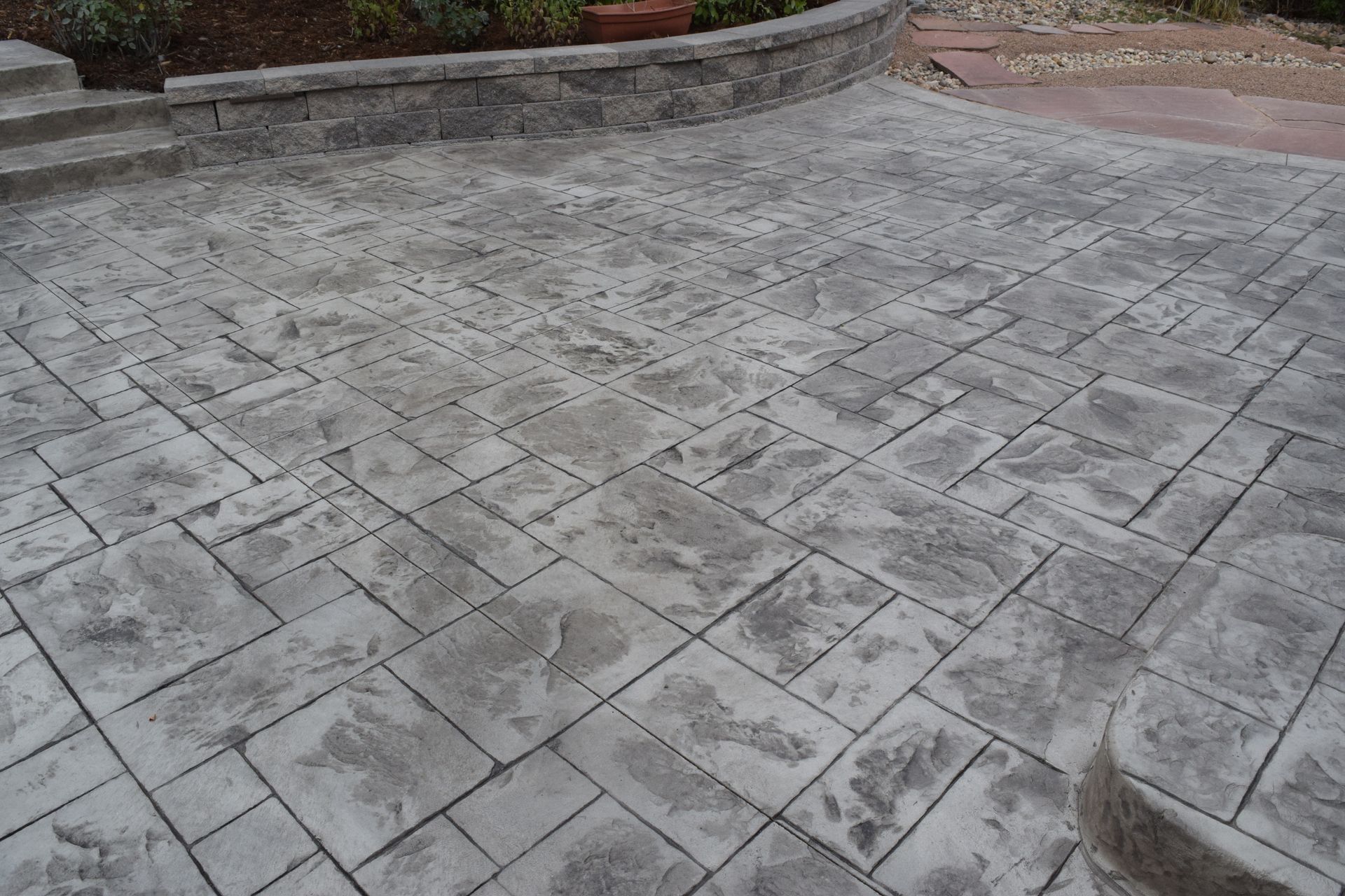 Gray stamped concrete patio with stone-like texture, leading to a stone wall and steps.