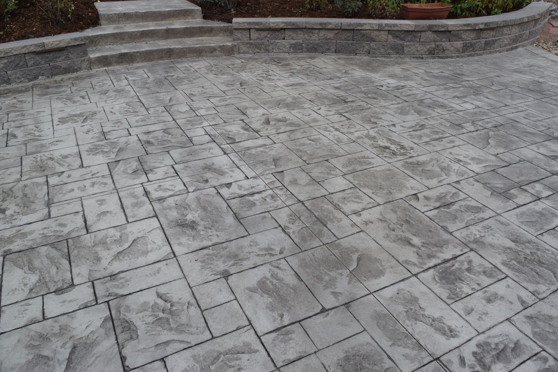 Gray stamped concrete patio with textured rectangular and square patterns, leading to steps and landscaping.