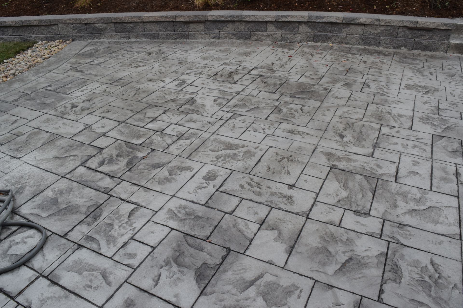 Gray, textured concrete patio with a stone pattern. A small, decorative retaining wall in the background.