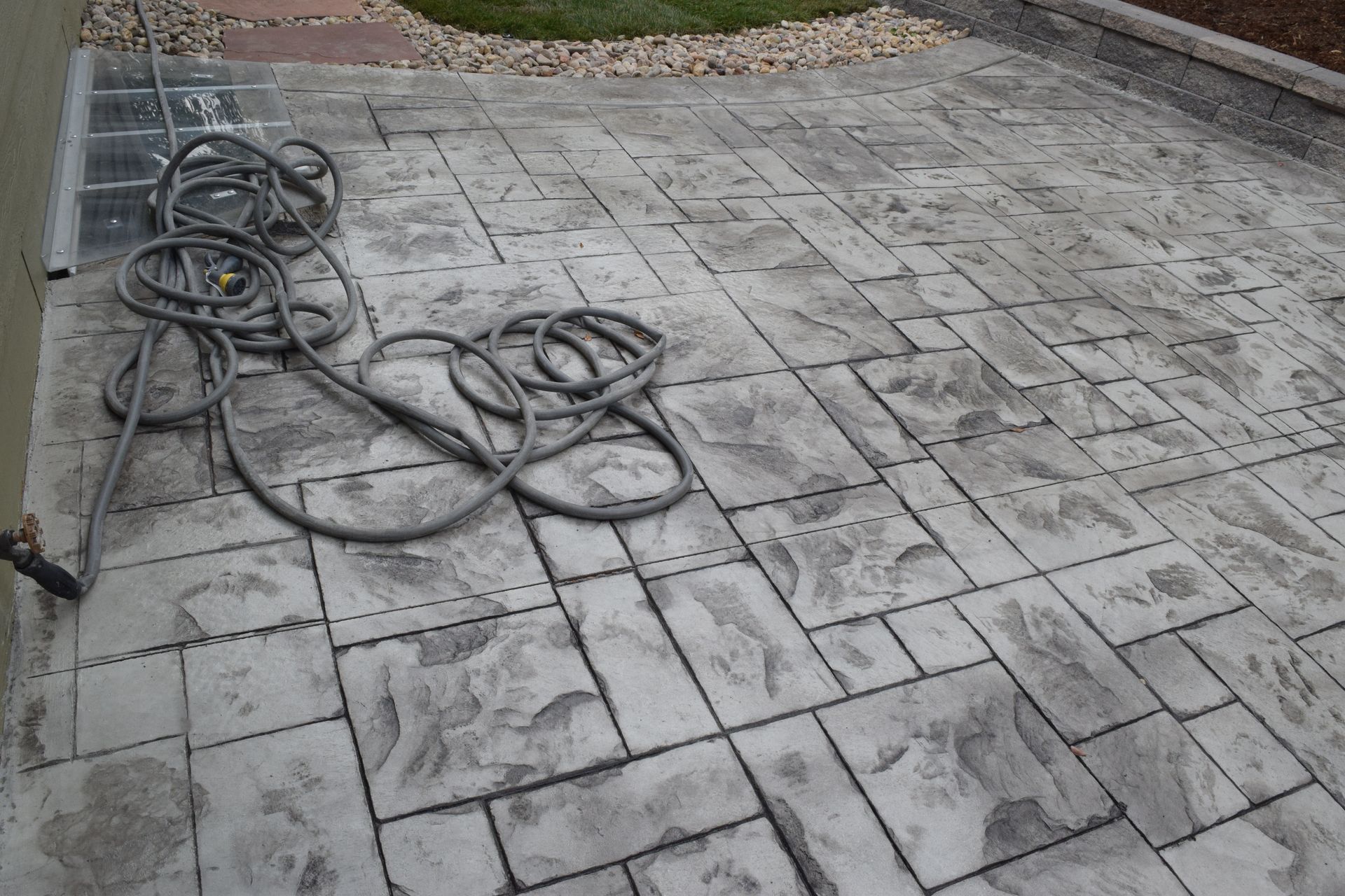 Gray, stamped concrete patio with a coiled hose.