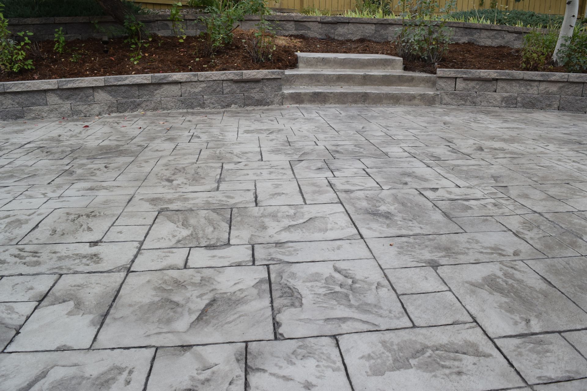 Stamped concrete patio with stone-like pattern, leading to steps and a raised bed.