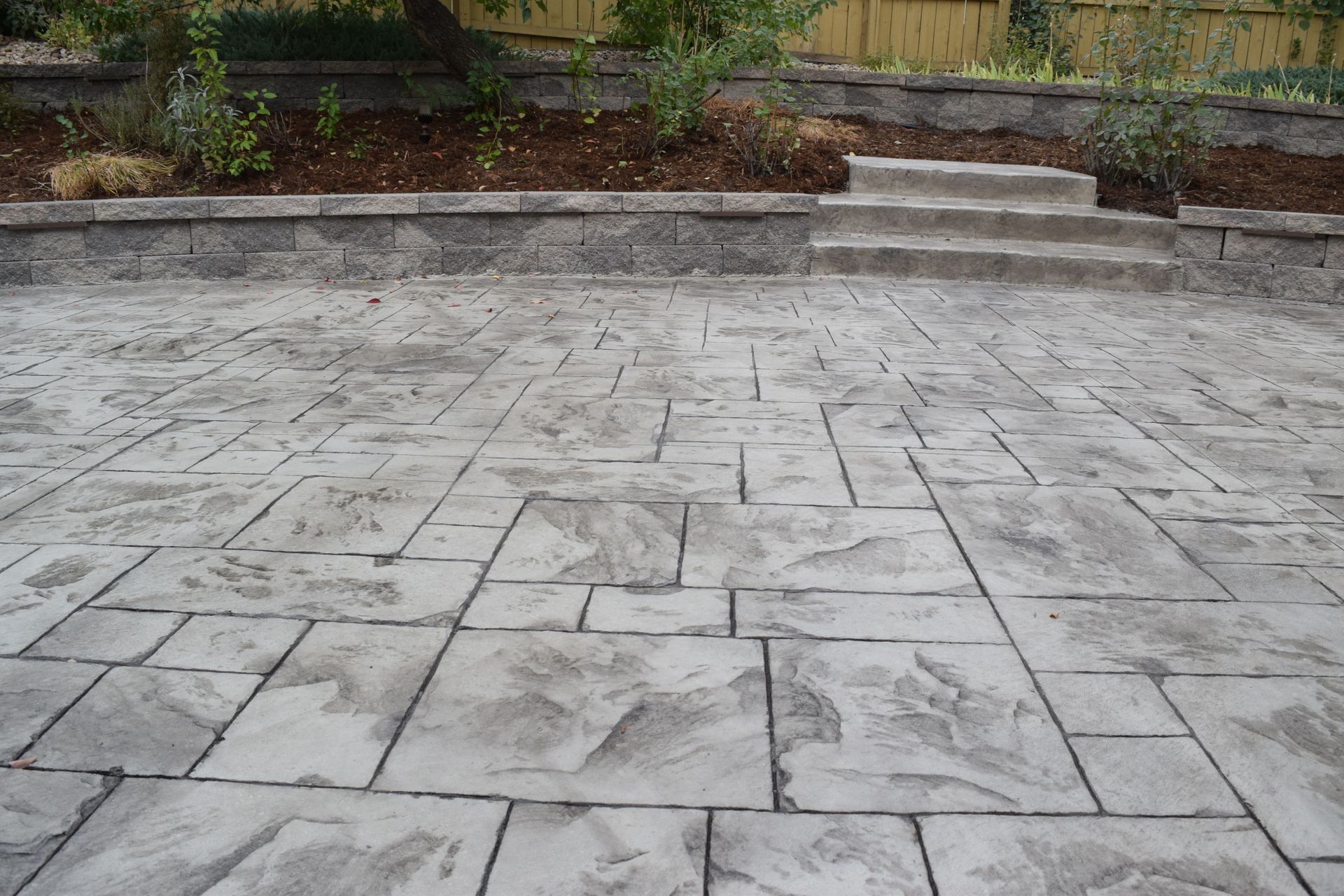 Concrete patio with a stone pattern, retaining wall, and steps.