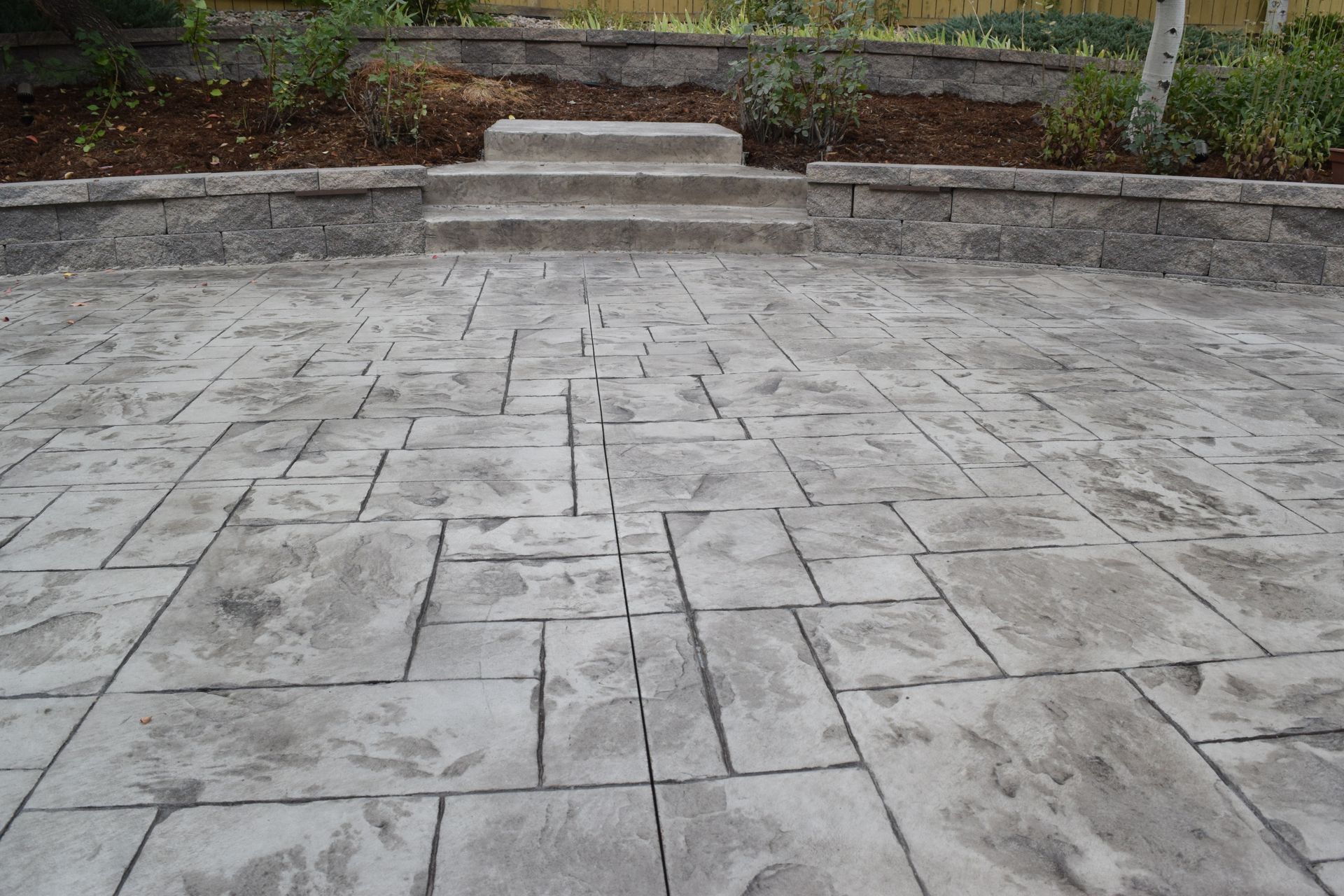 Stamped concrete patio with steps leading up to a garden area.