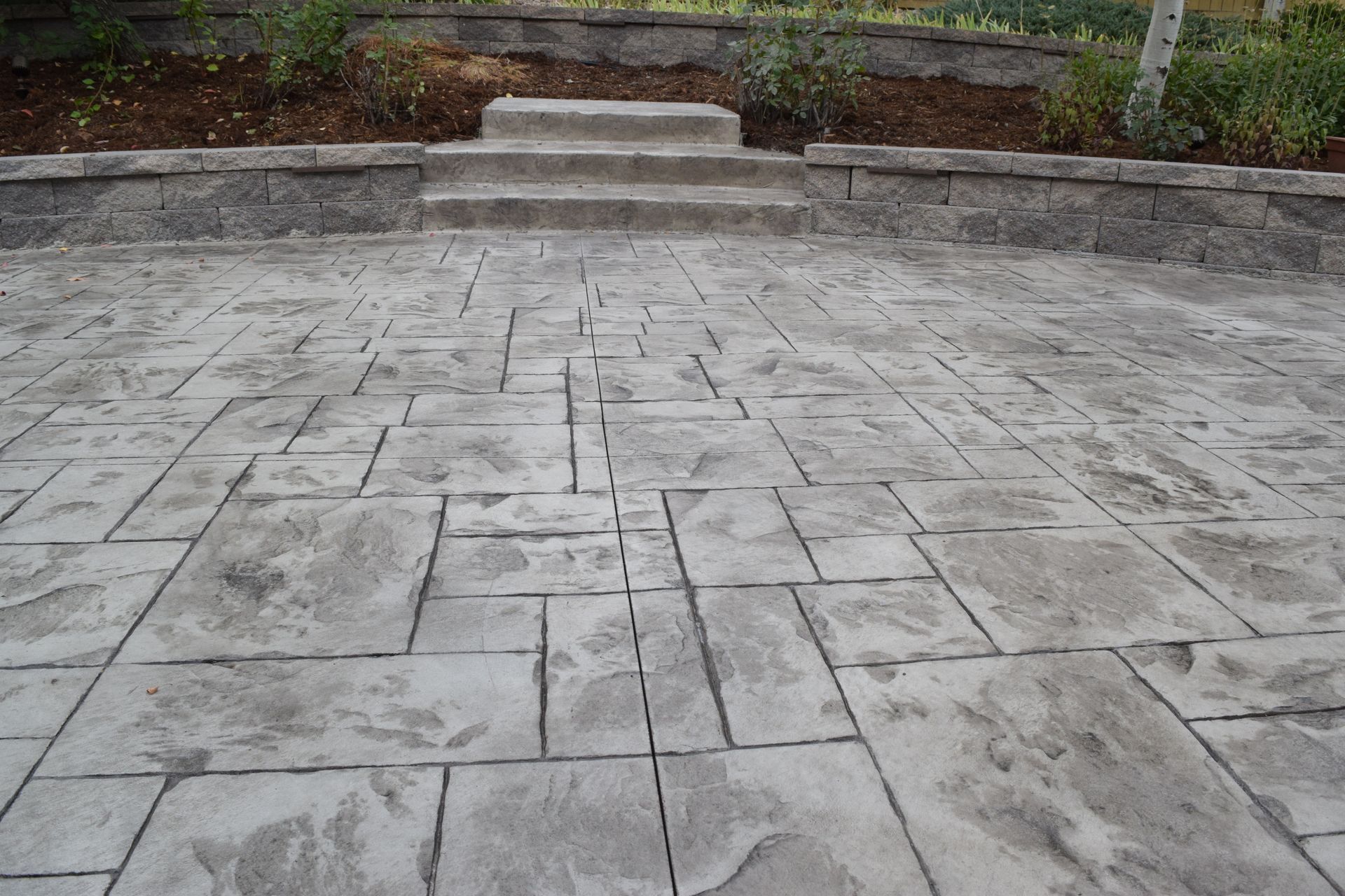 Gray stamped concrete patio with steps leading to a raised garden bed.