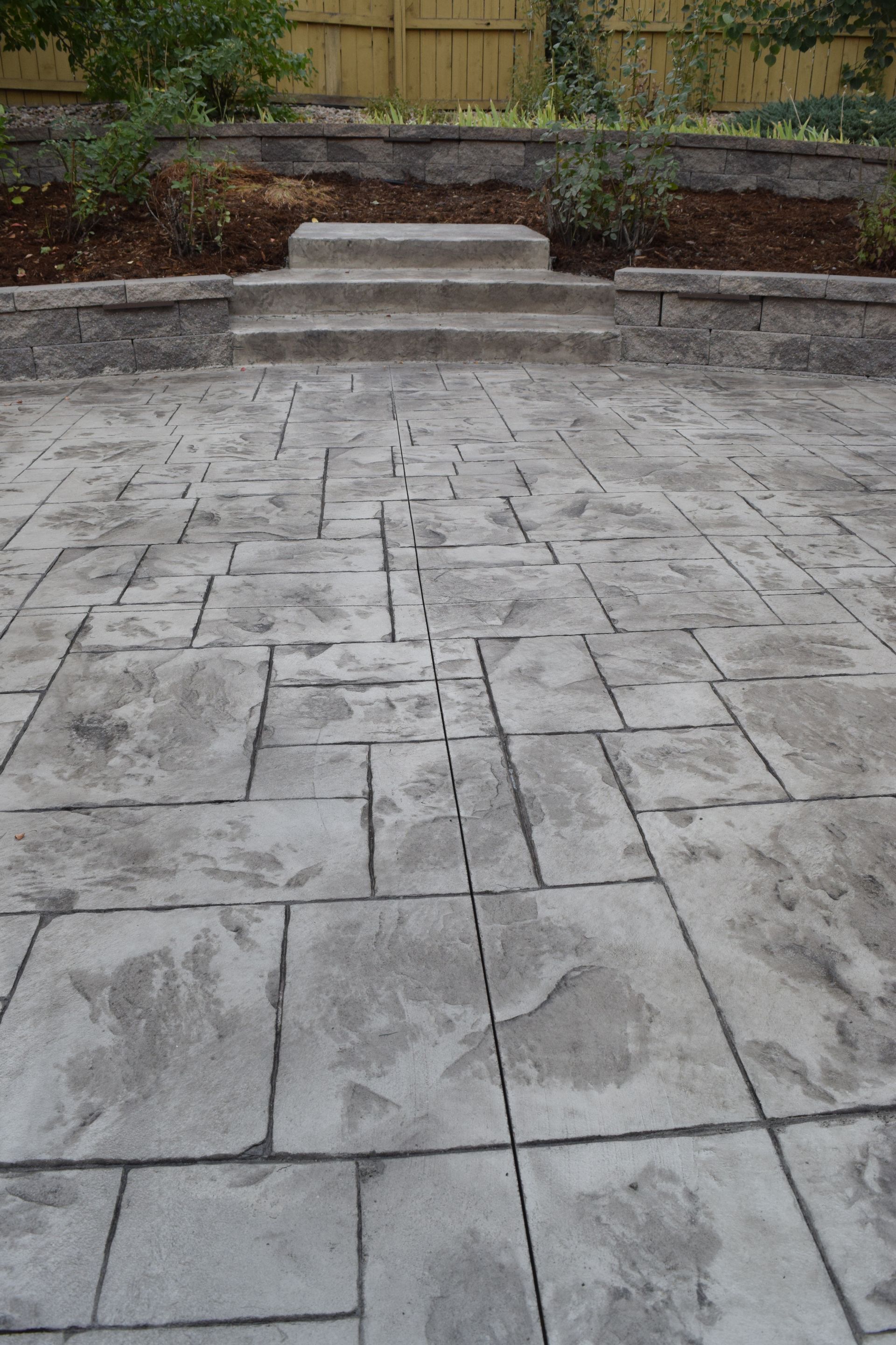 Stamped concrete patio leads to steps, small retaining wall, and backyard.