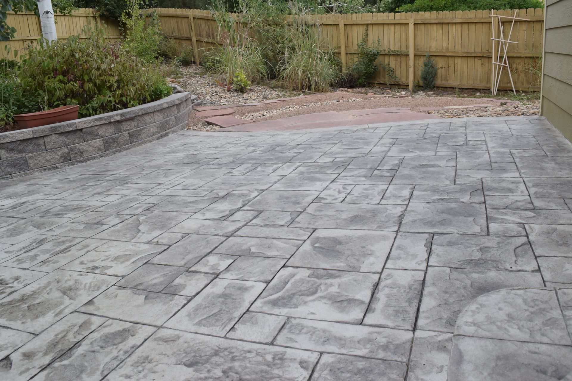 Stamped concrete patio with a gray stone pattern, next to a wooden fence and retaining wall.
